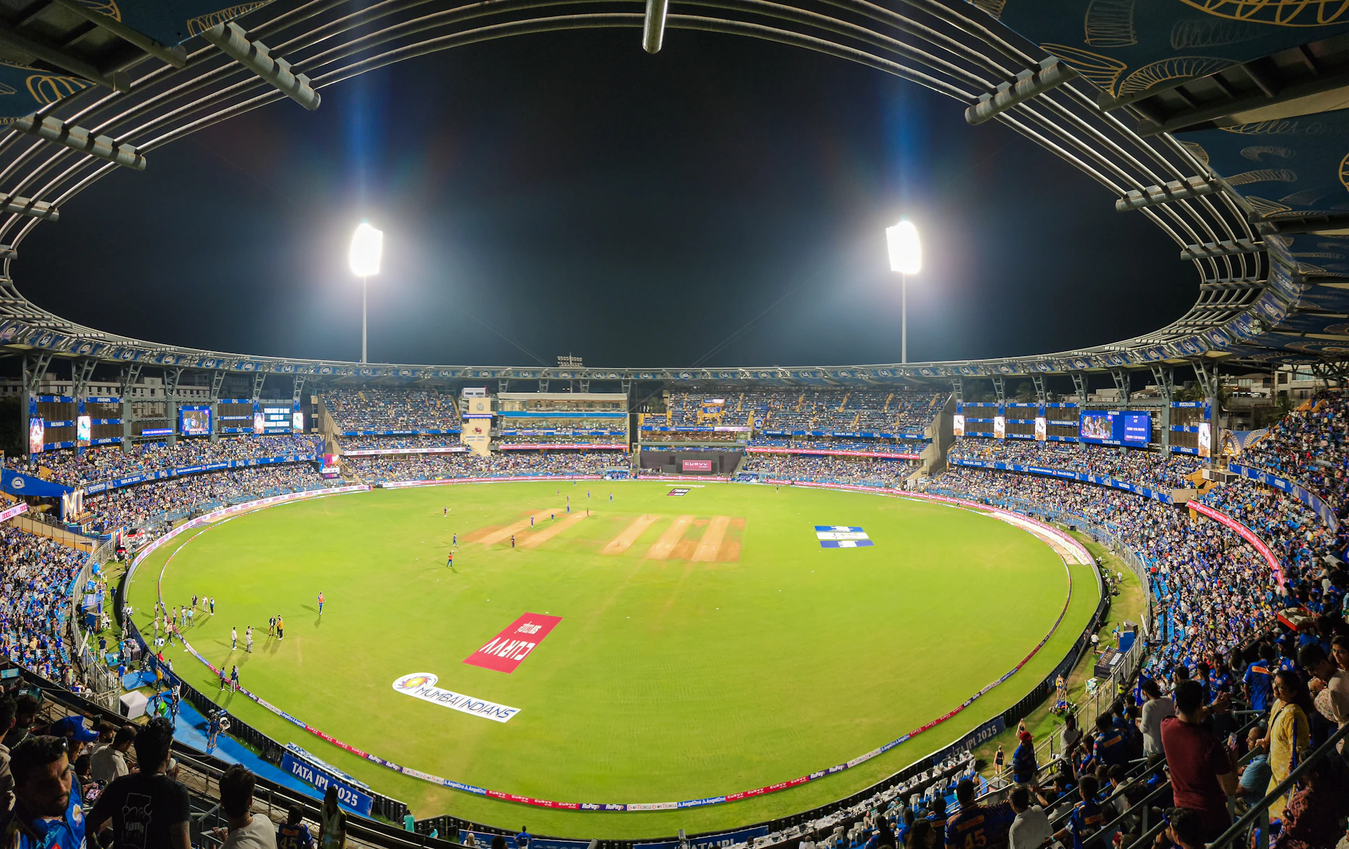 A cricket stadium is filled with spectators at night.