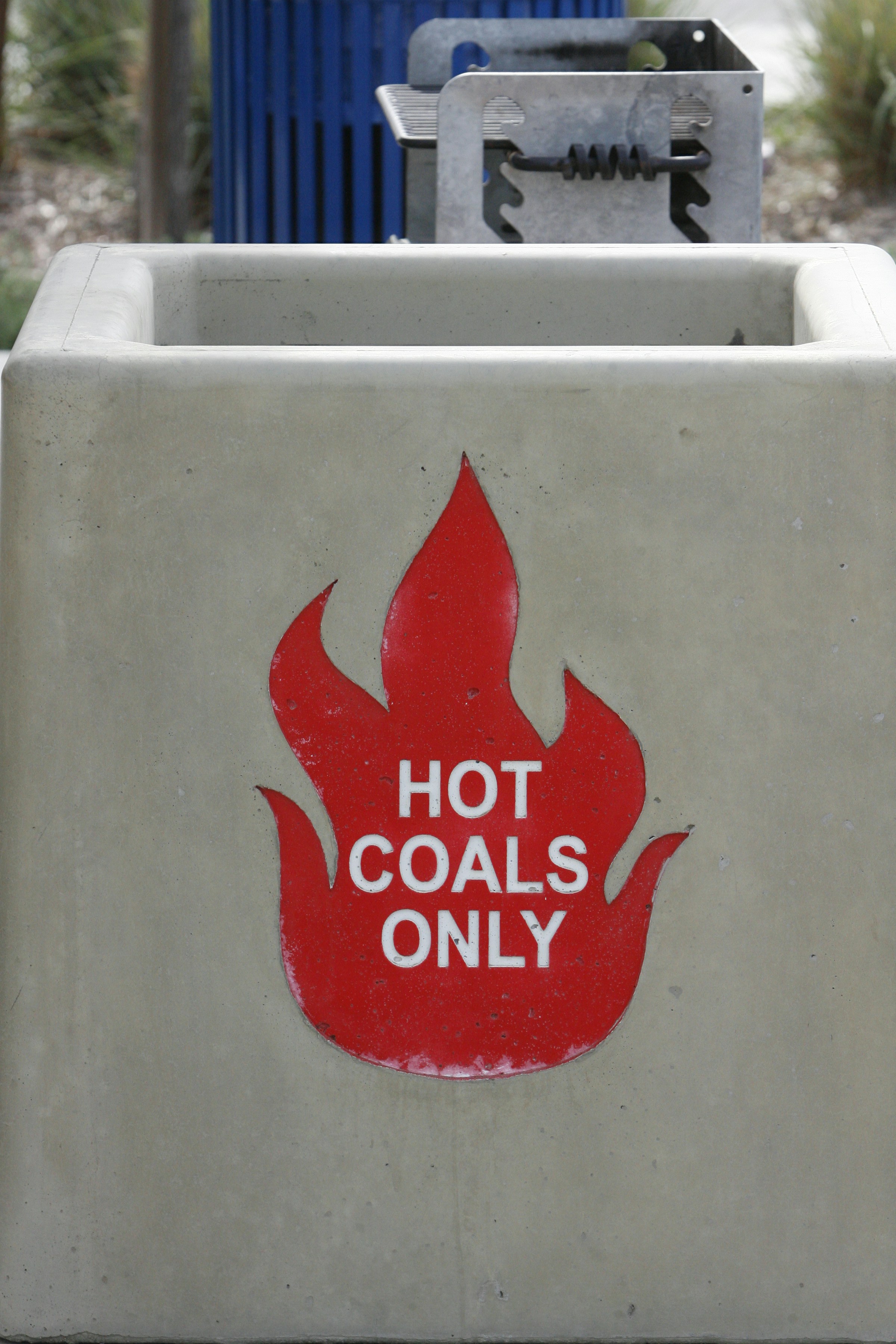 A concrete trash can with hot coals sign.