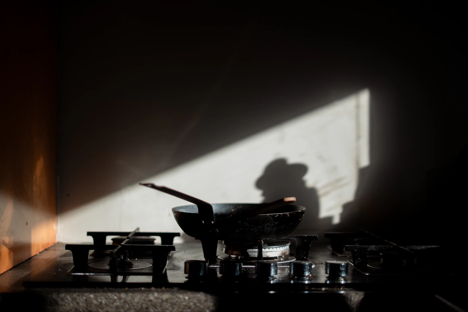 Pan on a gas range under a raking shaft of light with a cast shadow on the wall