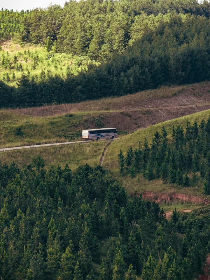 A coach travelling along a road across green, forested hills.