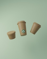 Three recyclable coffee cups floating on a green background.