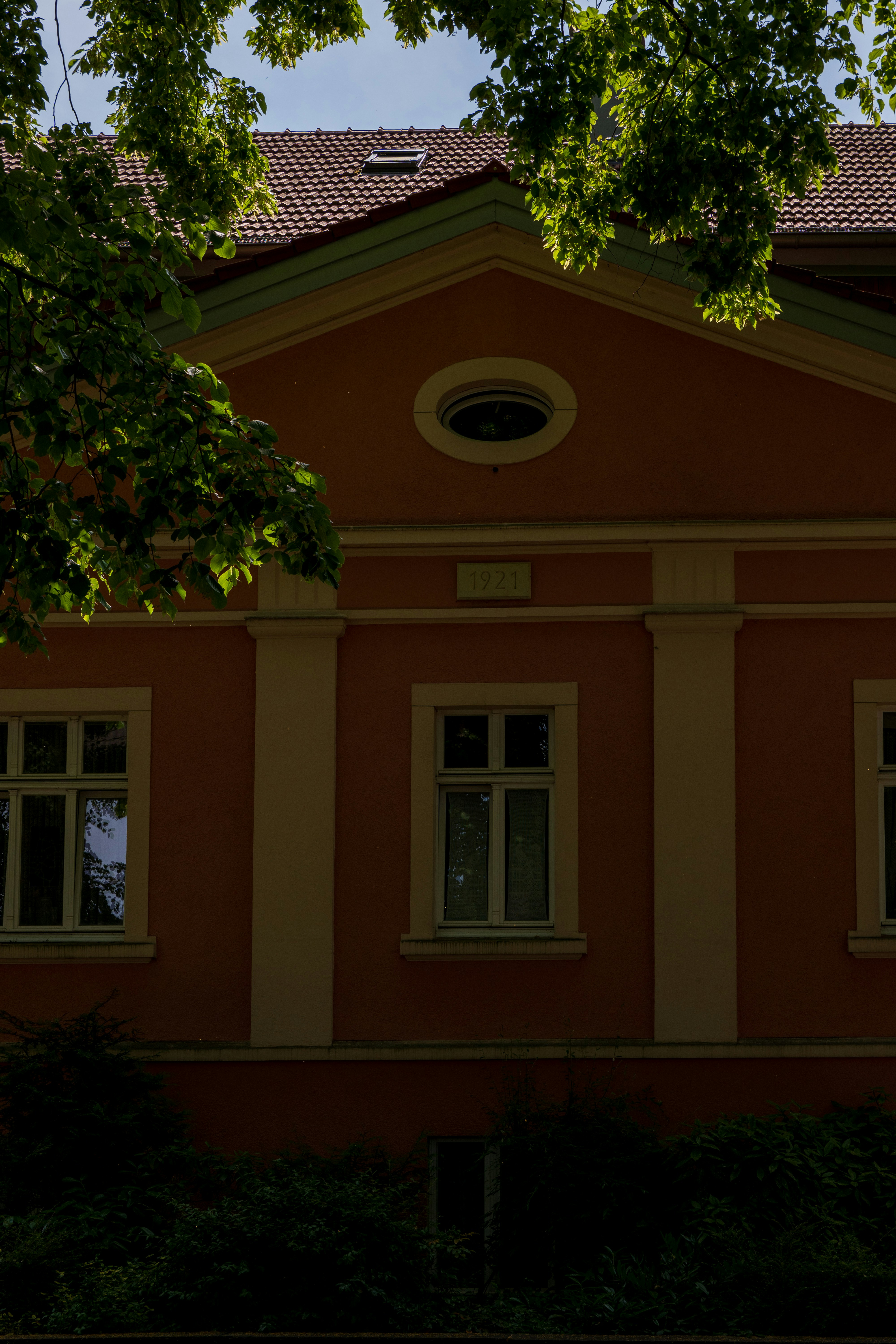 An orange building is framed by green foliage.