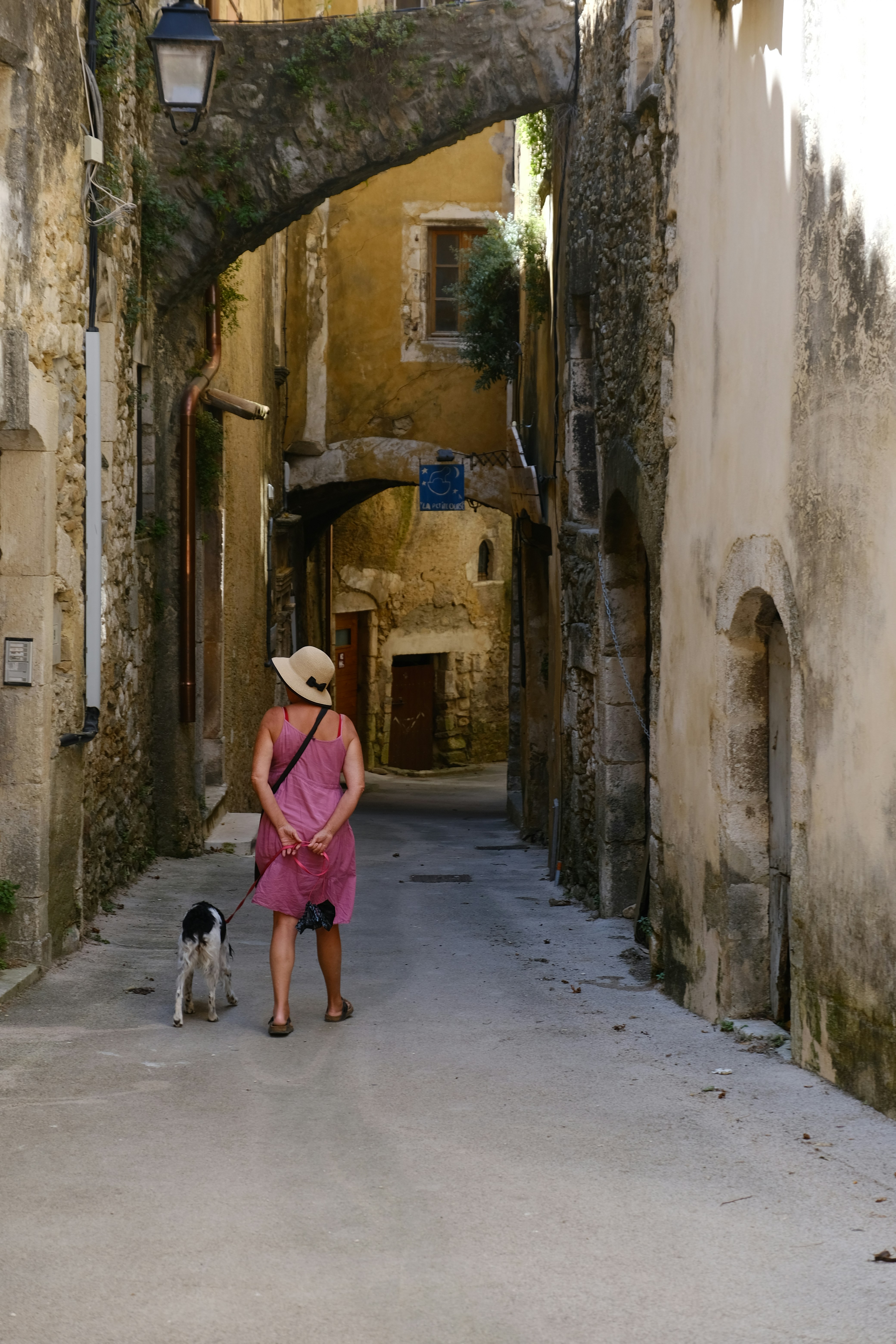 Woman walks a dog down a narrow, arched alleyway.