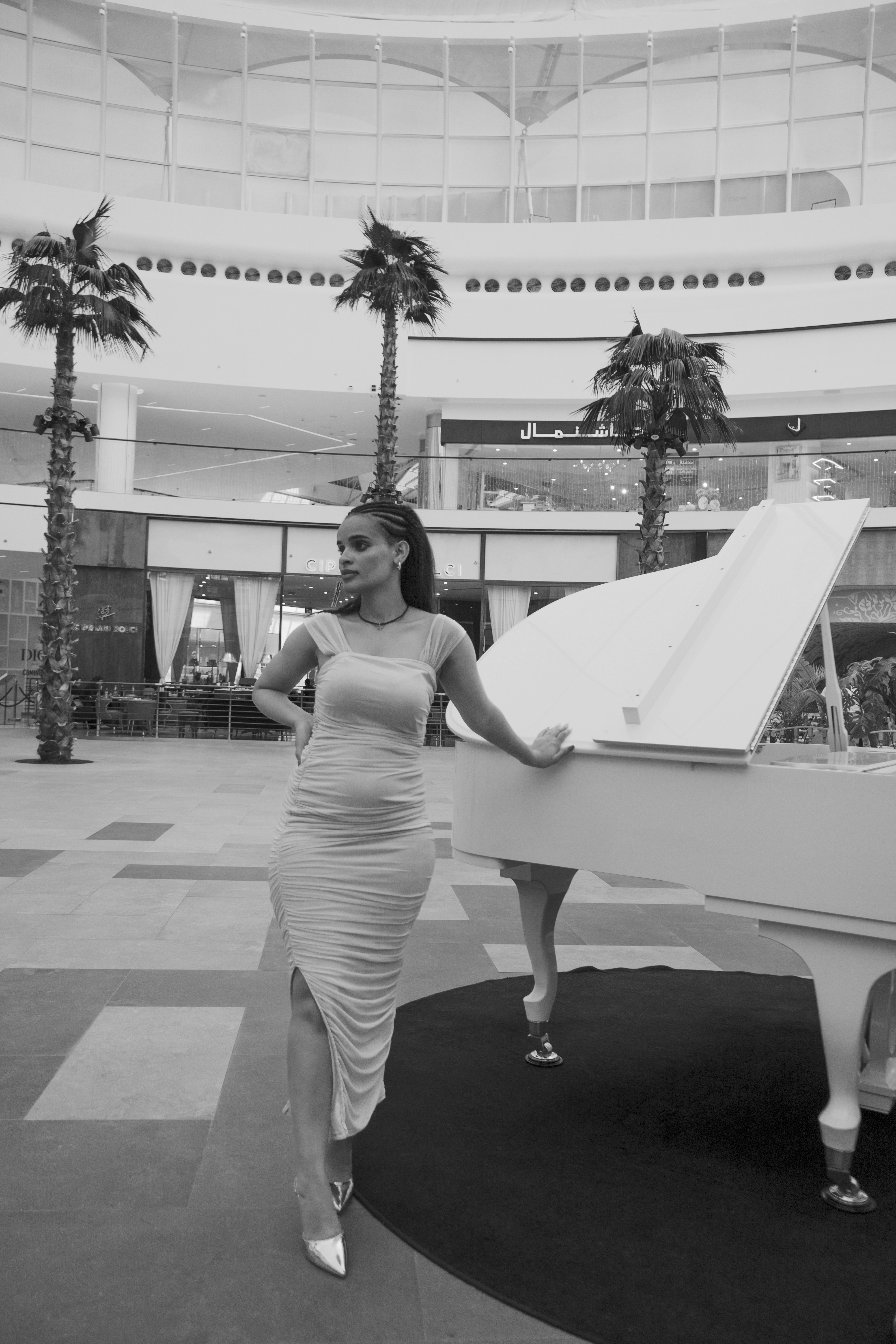 Woman poses elegantly beside a white piano.