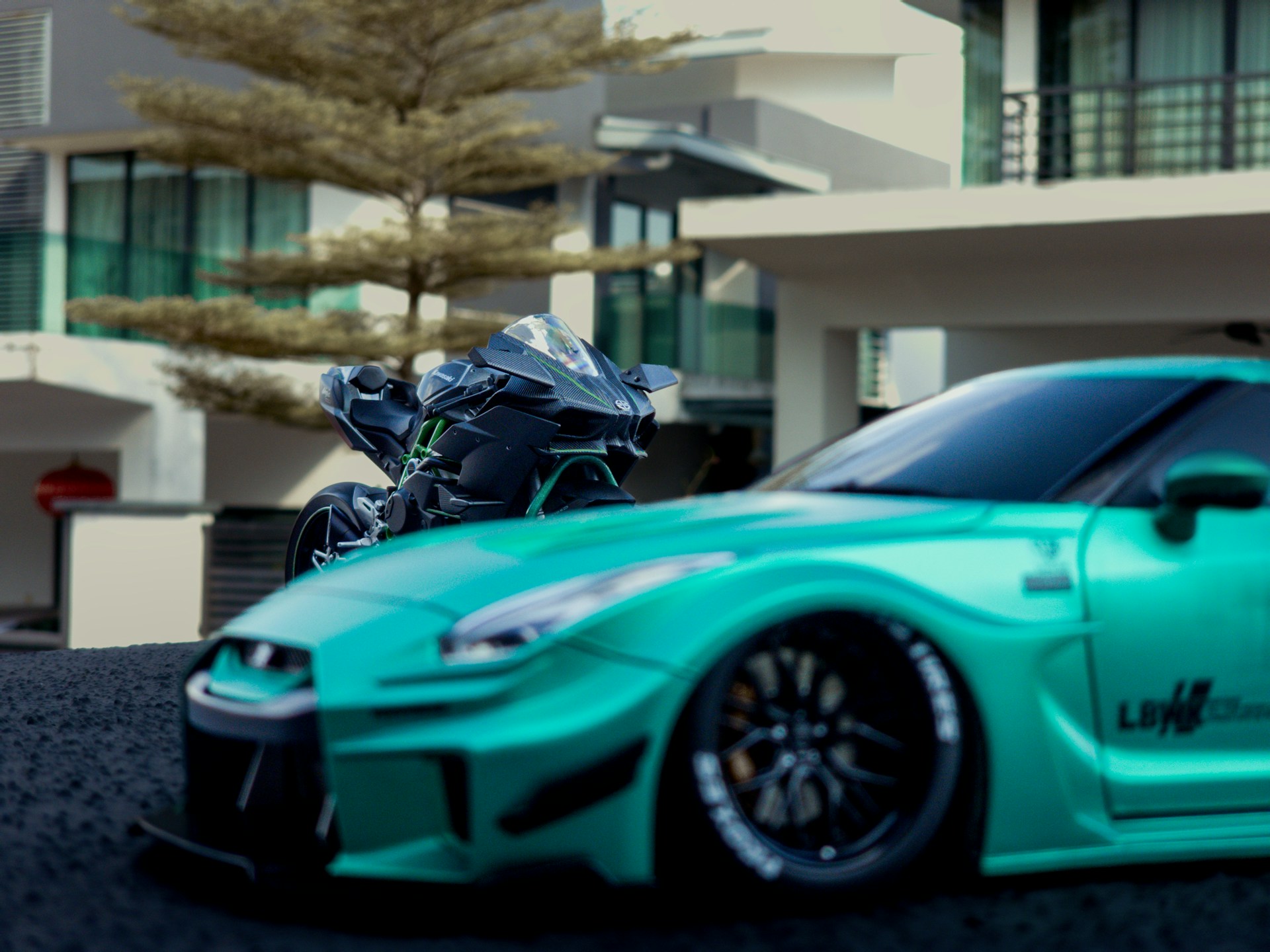A teal sports car and a motorcycle are parked.