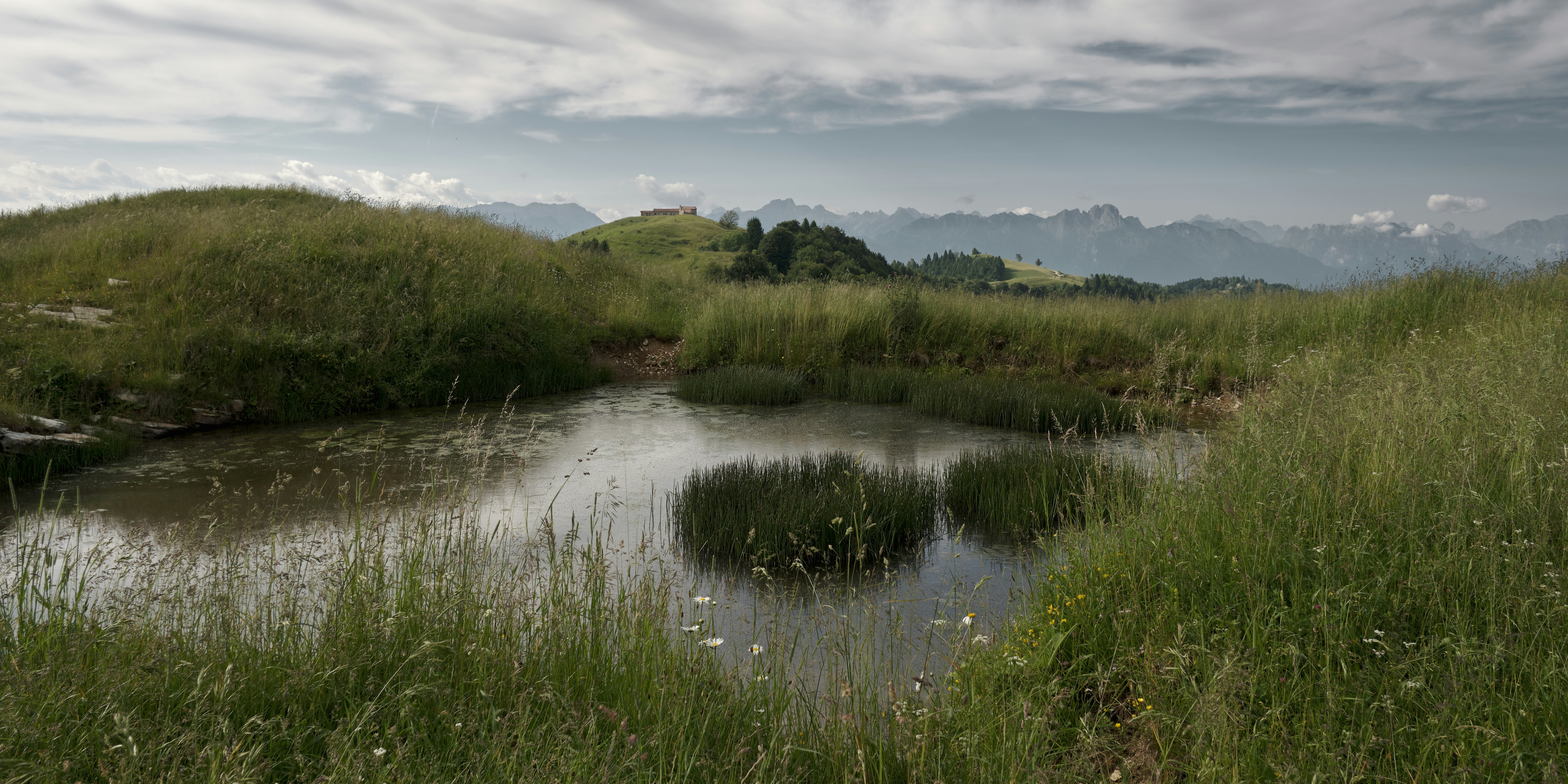 Uno stagno circondato da colline erbose e montagne lontane.