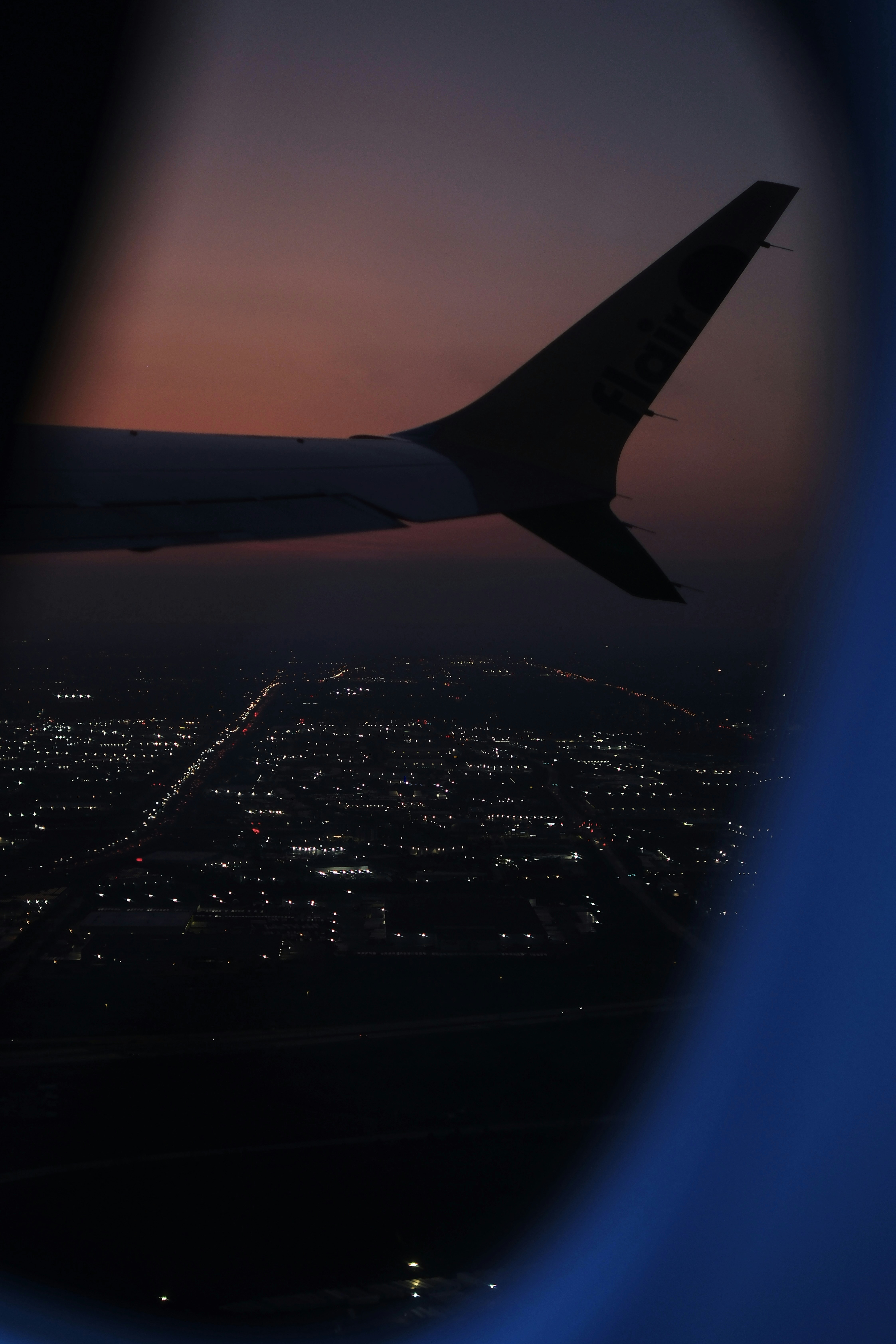 Airplane wing and city lights during sunset.