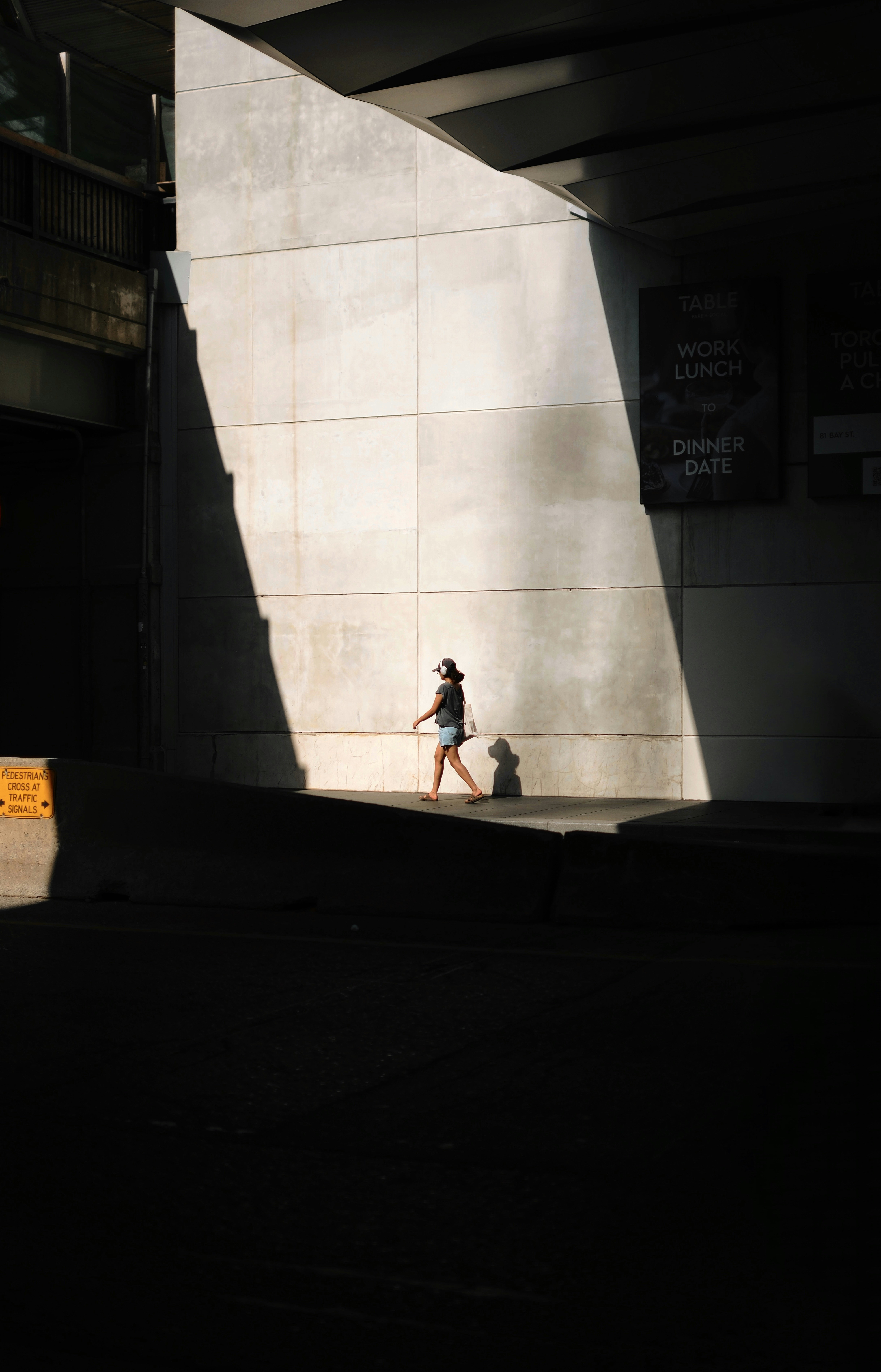 A person walks in sunlight under a concrete structure.