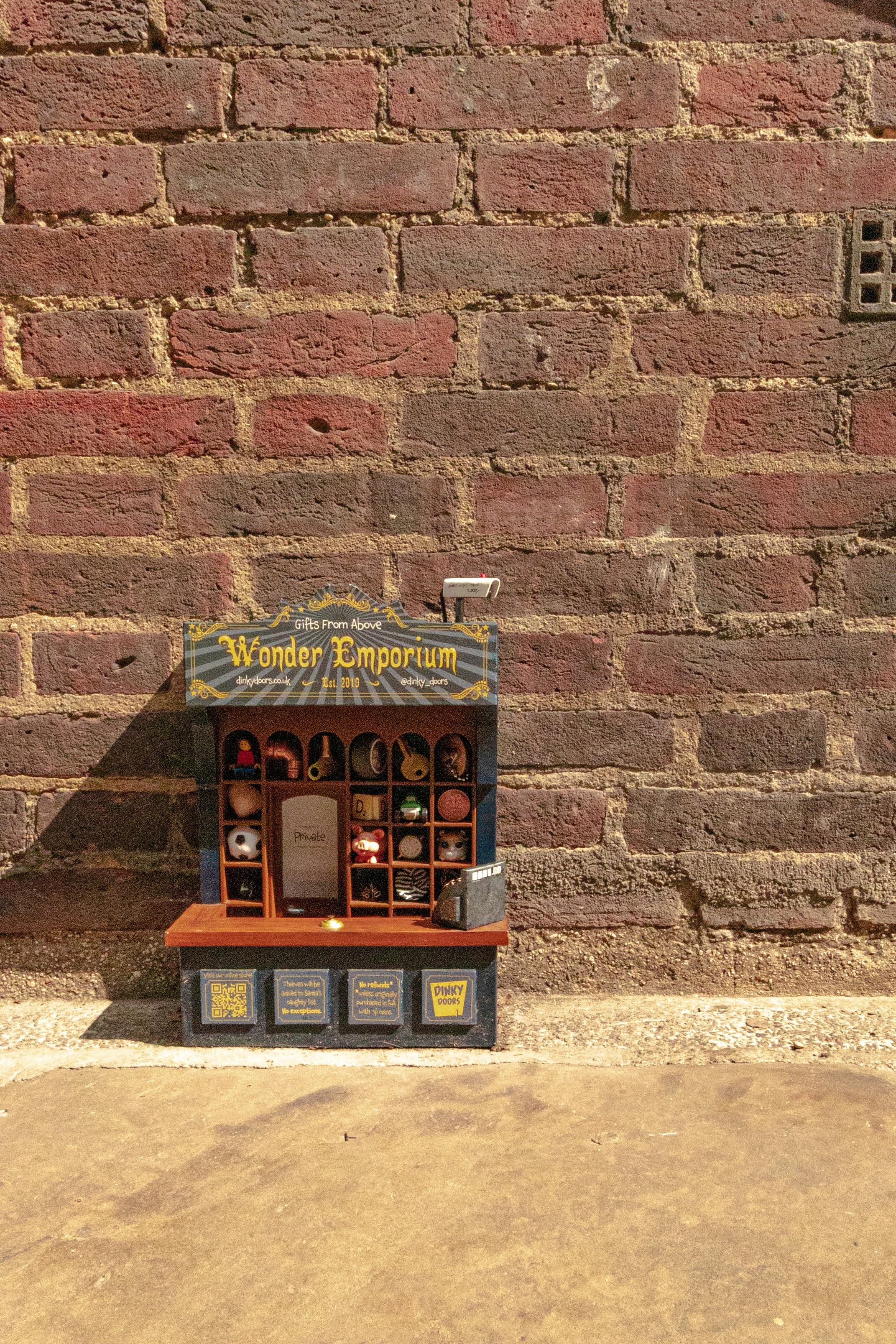 Miniature shop stands in front of a brick wall.