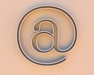 An "at" symbol on a beige background.