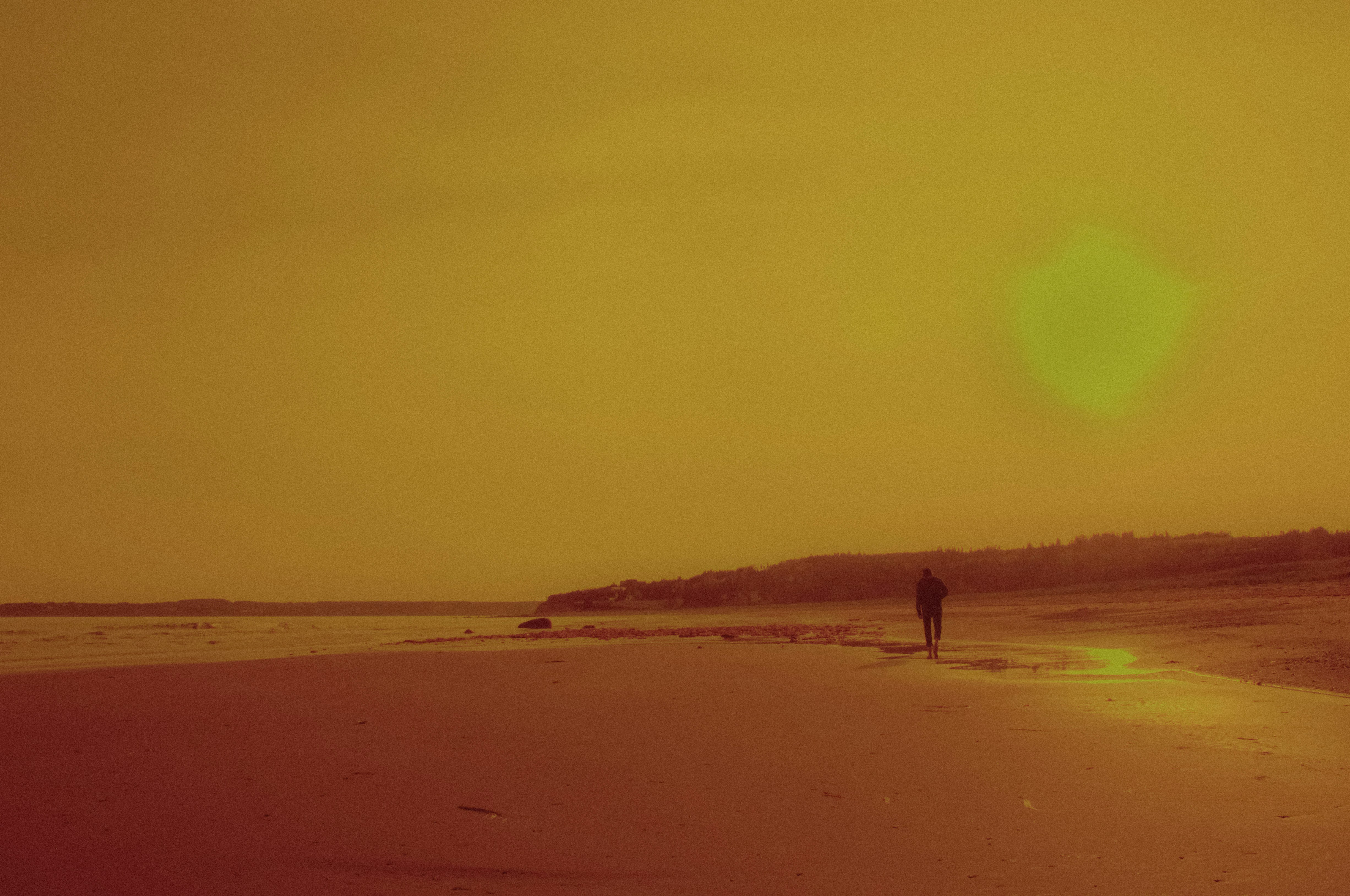 Eine einsame Gestalt spaziert bei Sonnenuntergang an einem Strand entlang.