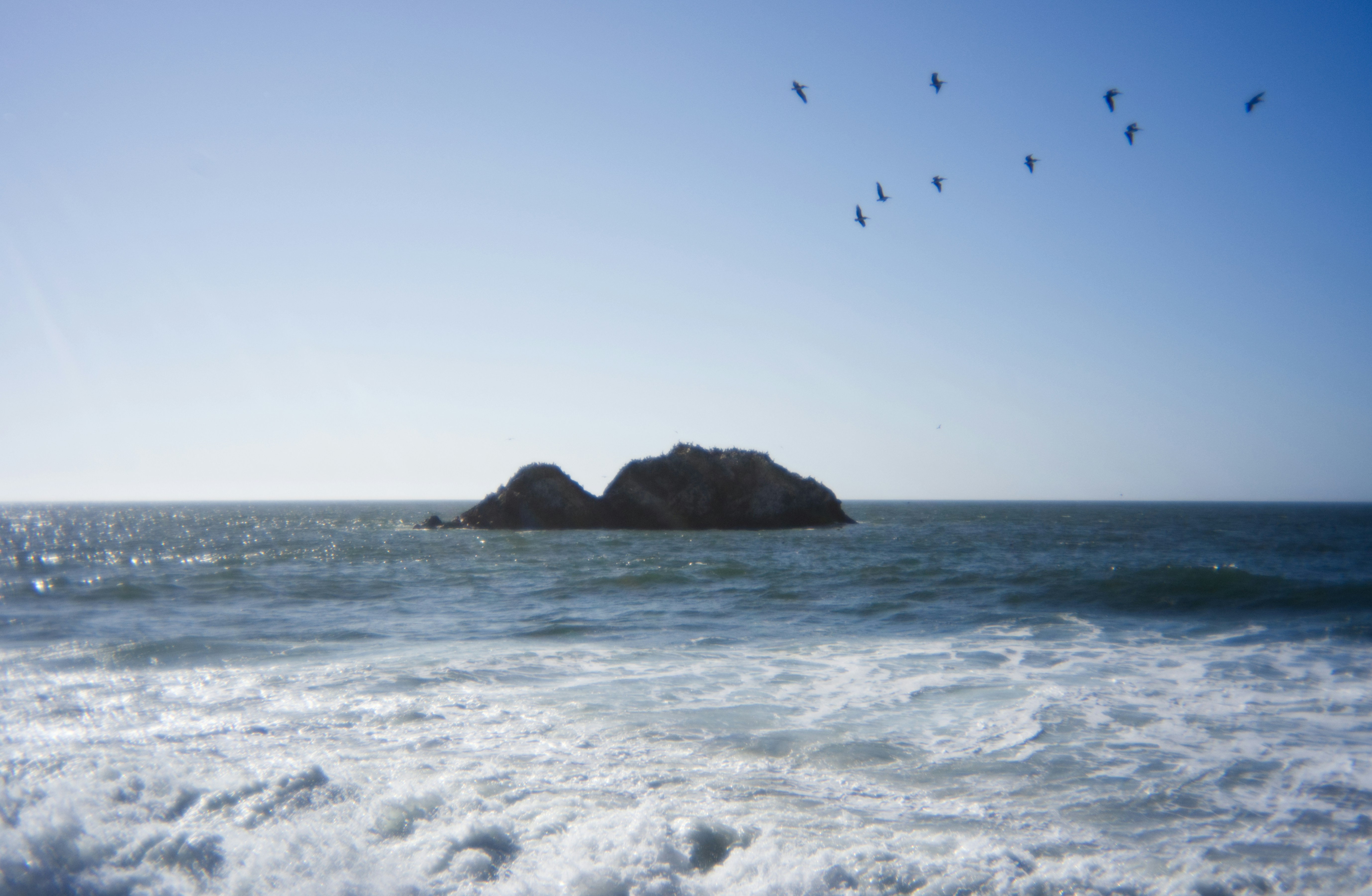 Birds fly above the ocean and a rock formation.