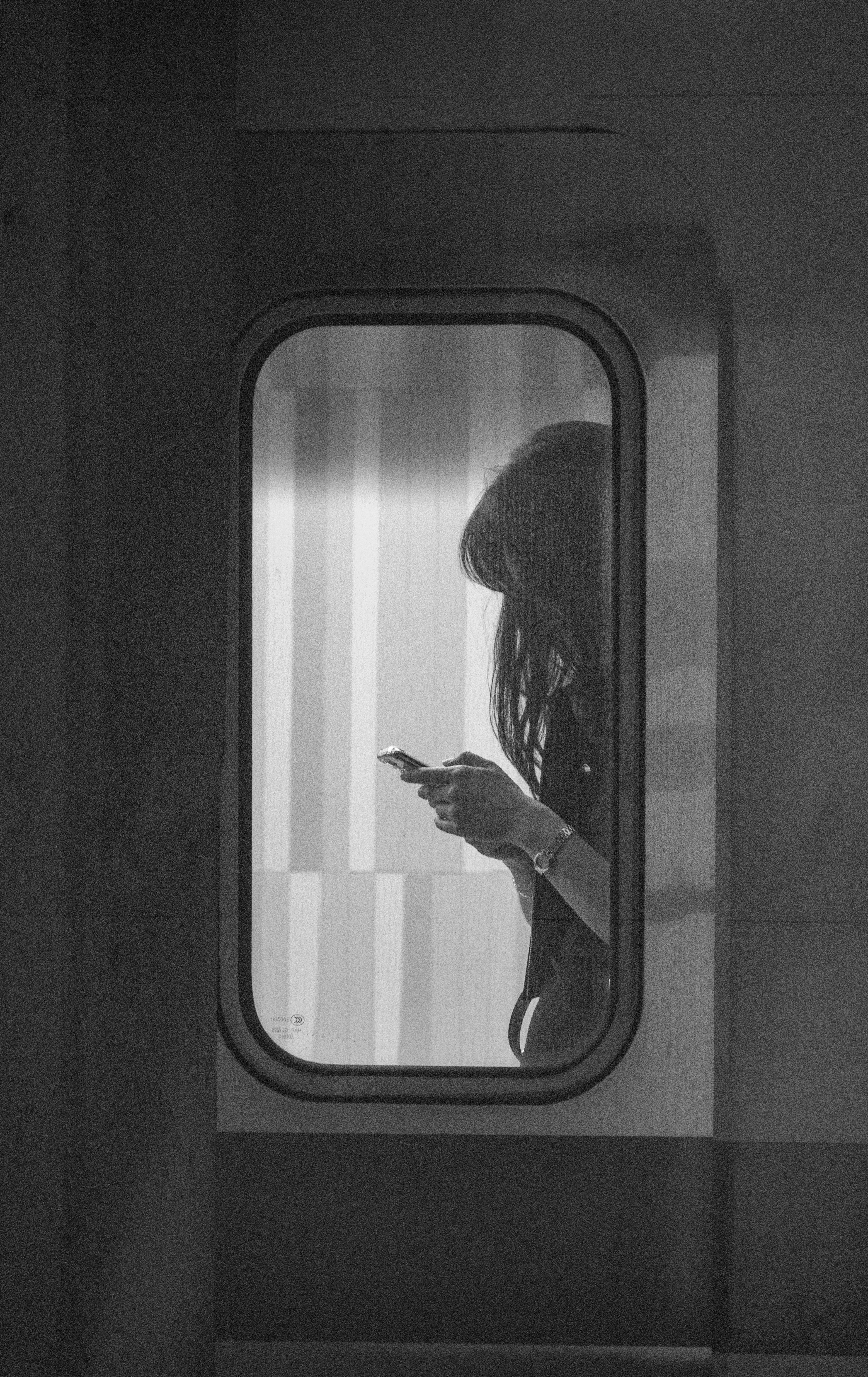 A woman looks at her phone through a window.