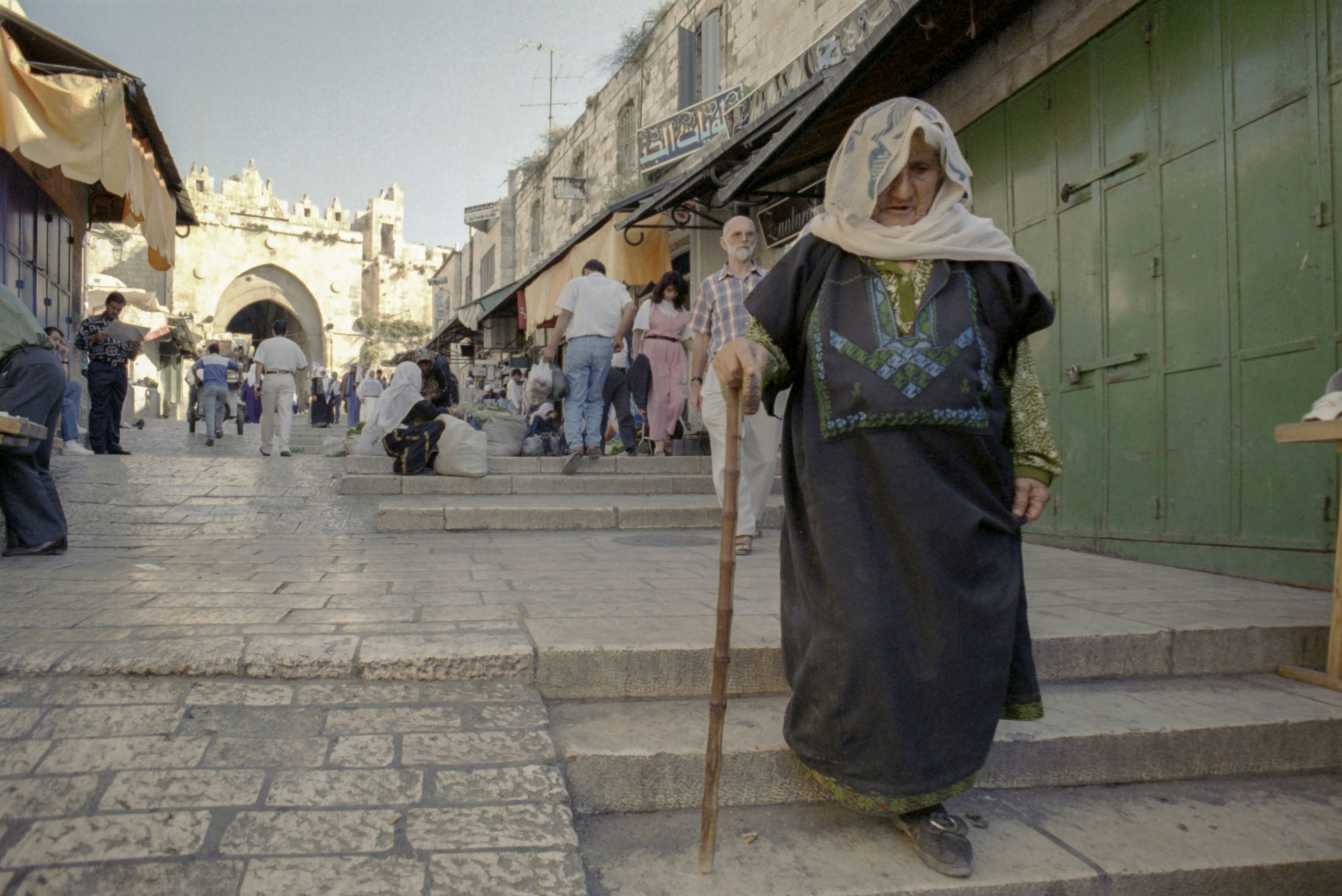 A woman walks on a street with a cane.
