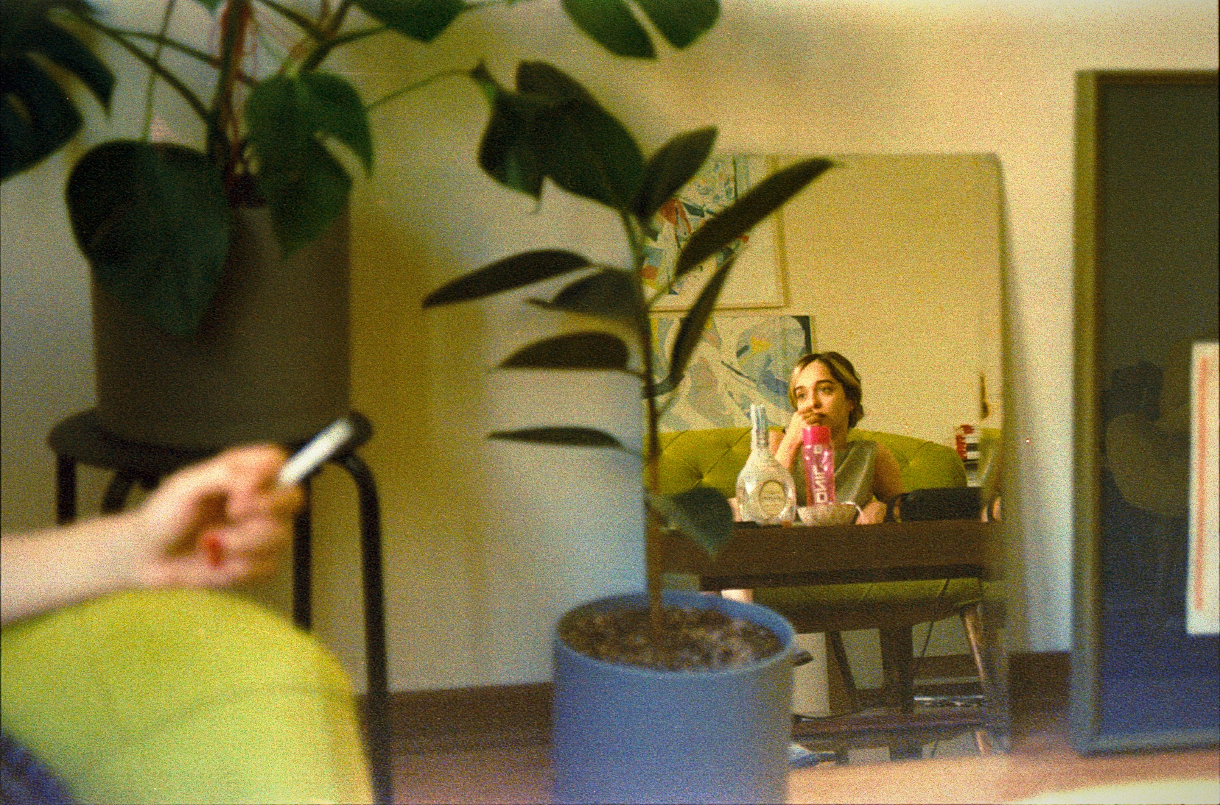 Person smoking, reflected in a mirror with plants.