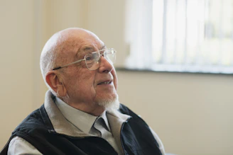 An elderly man wearing glasses gazes upwards
