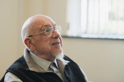 An elderly man wearing glasses gazes upwards