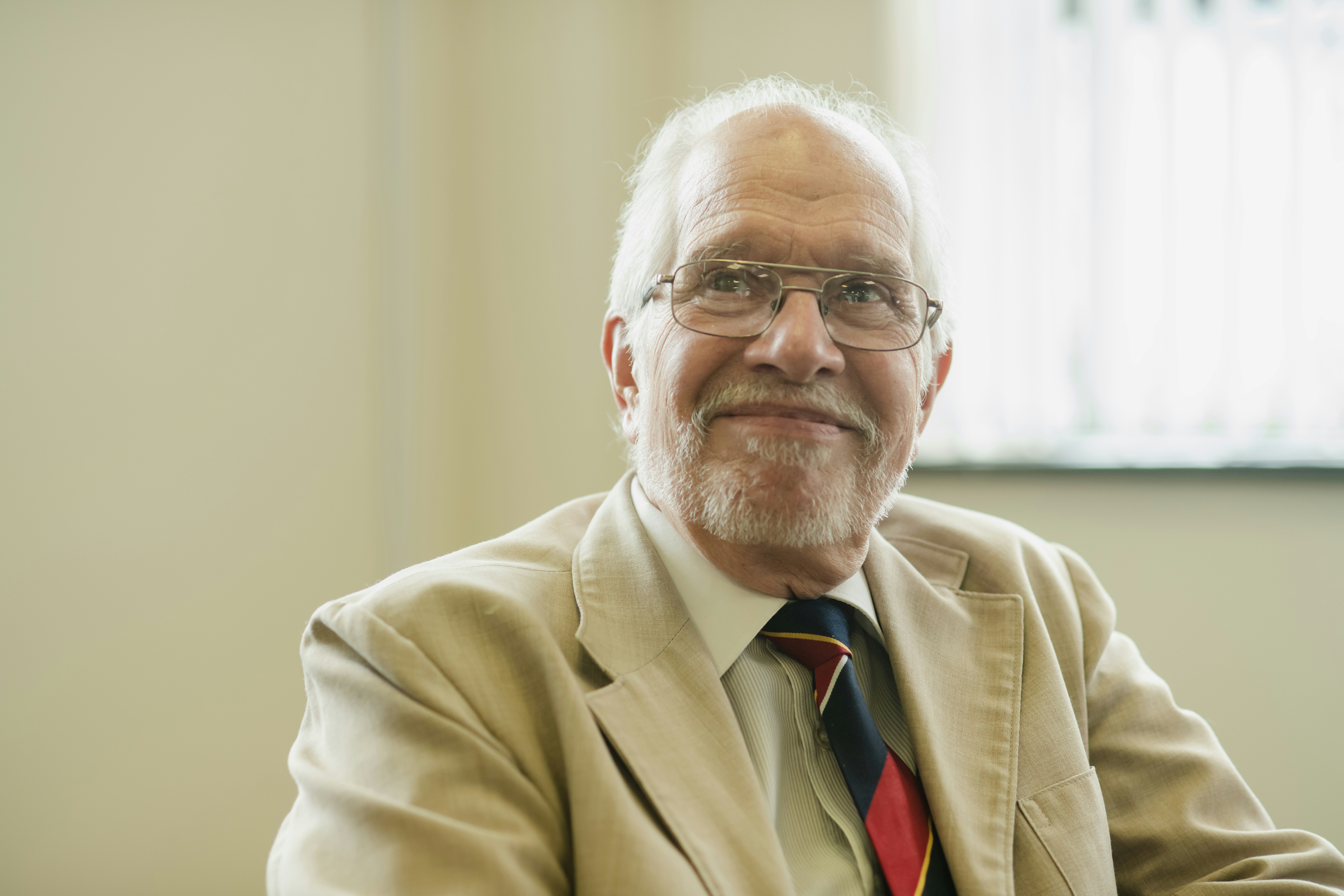 A smiling older man in a blazer and glasses.