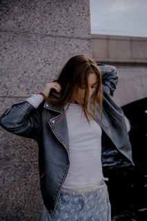 Young woman adjusting her jacket near a stone wall