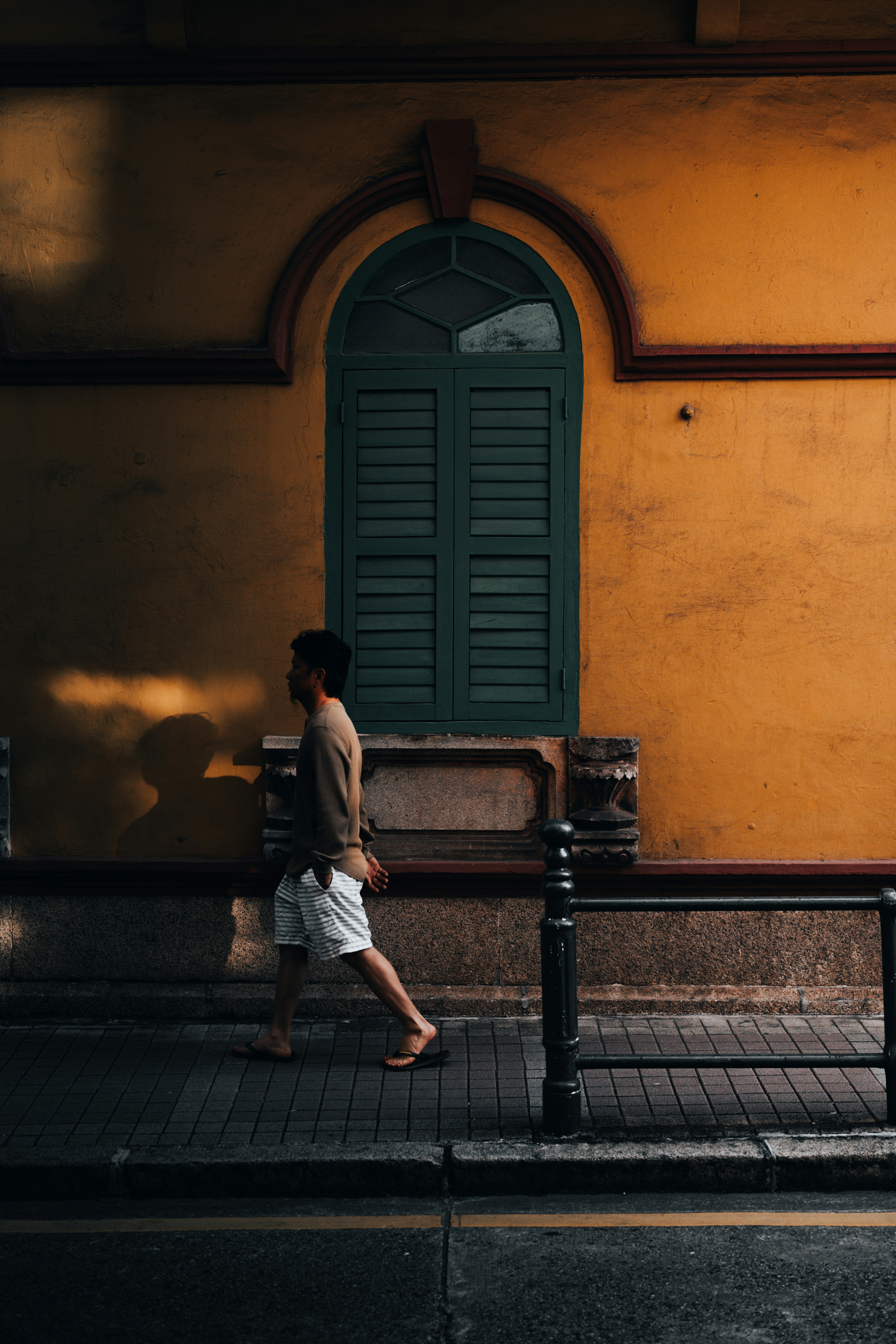 A man walks past a textured yellow building.