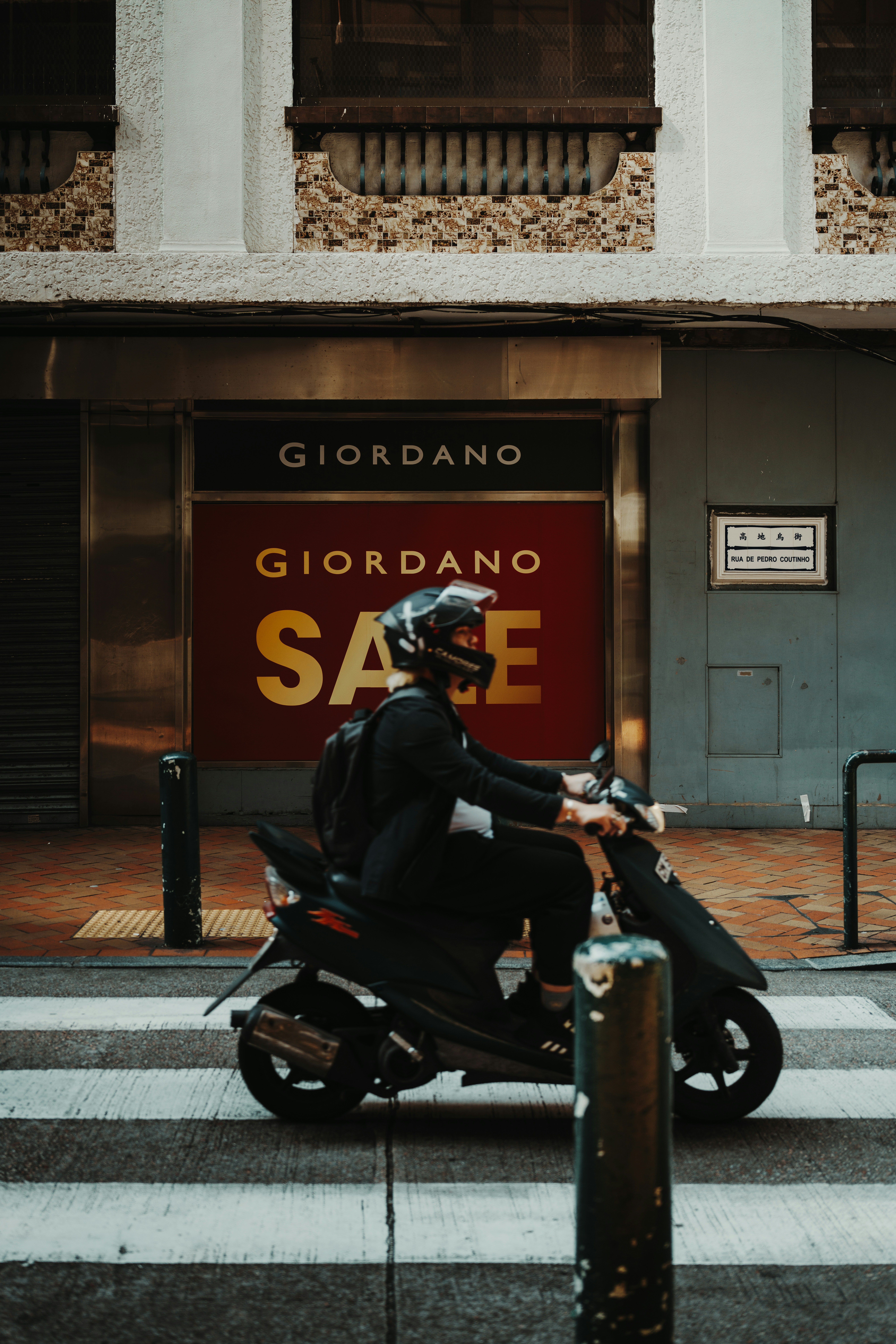 A person rides a scooter past a "sale" sign.
