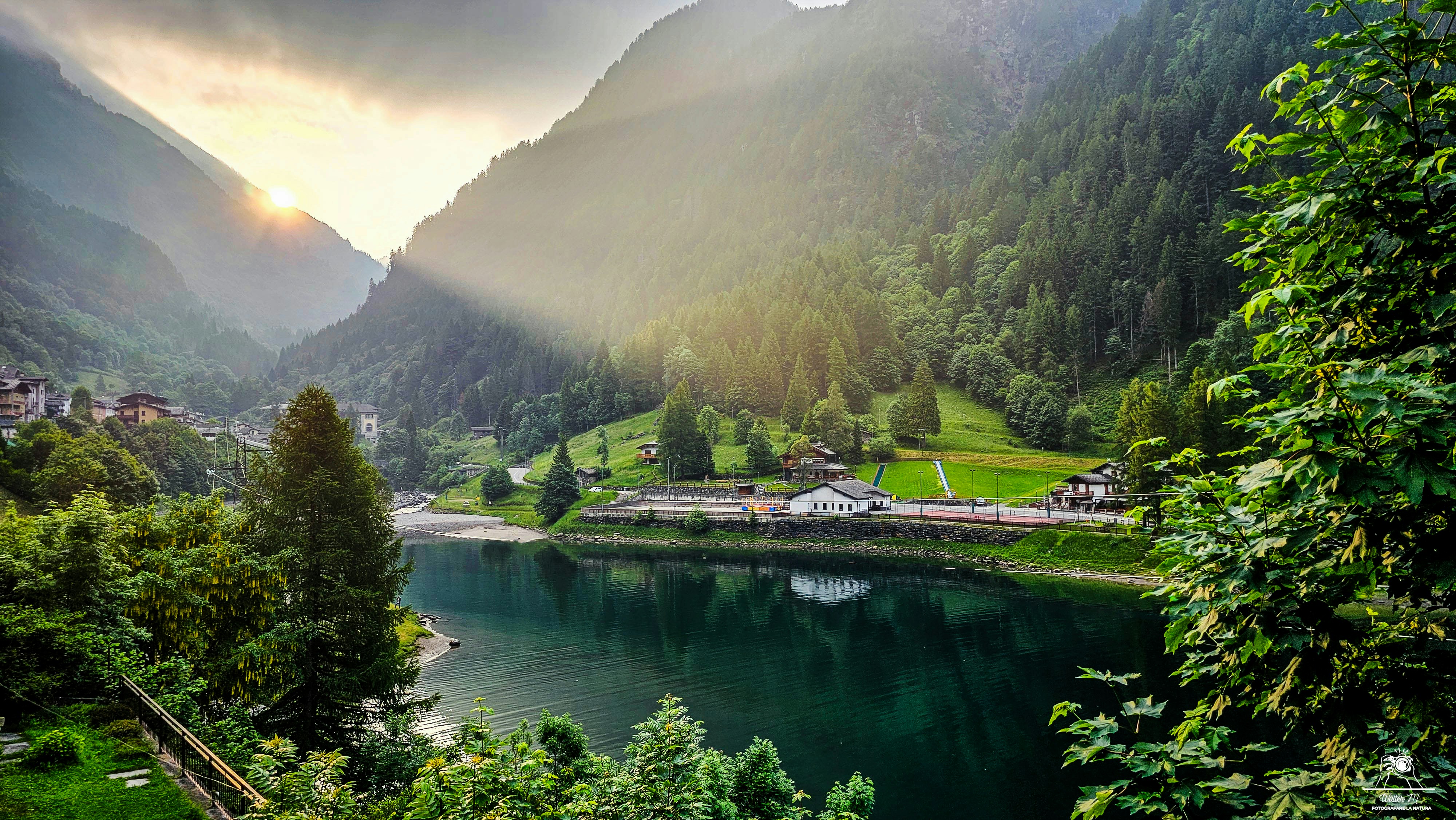 A serene lake reflects lush green mountains and sunshine.