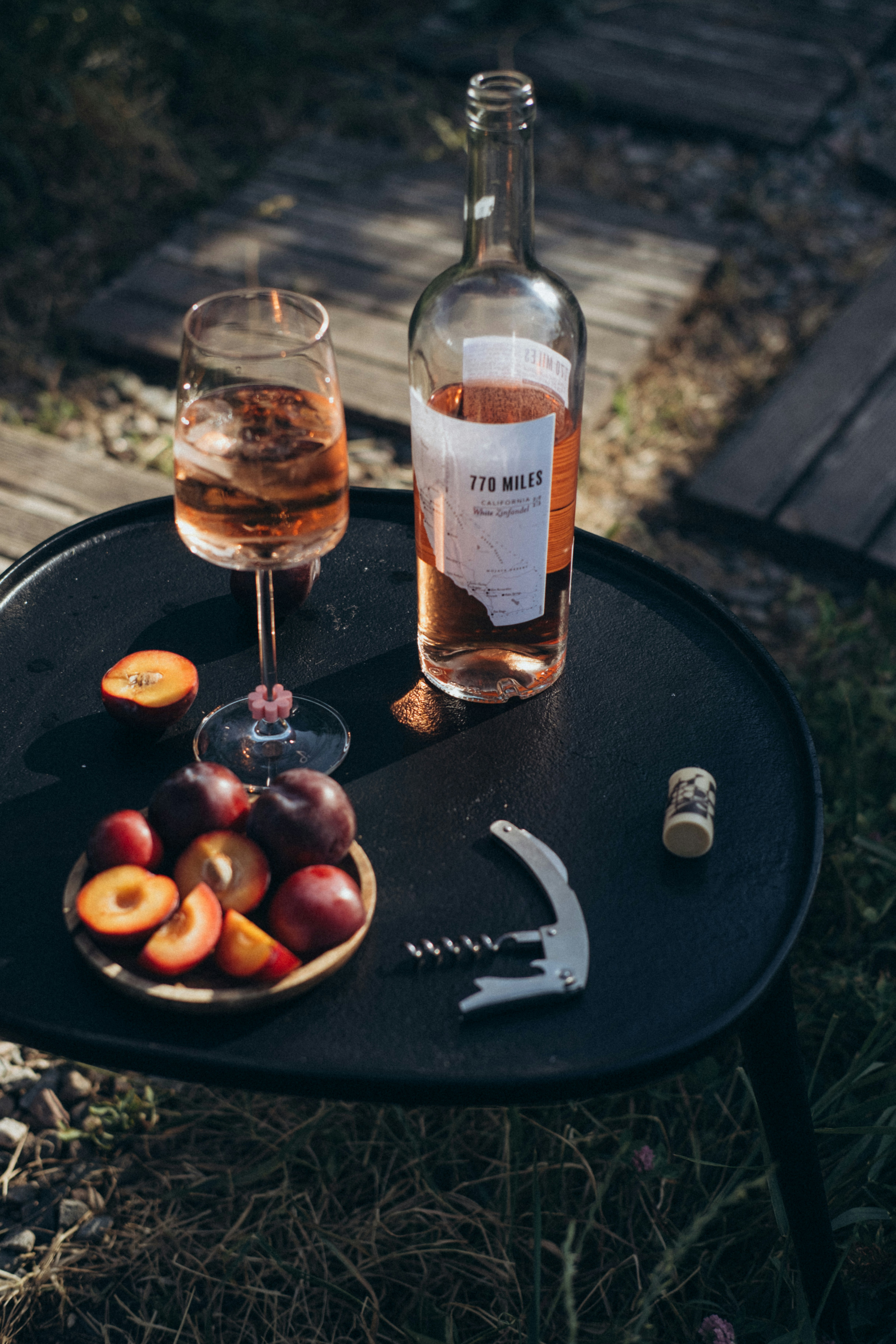 Wine, plums, and a corkscrew on a small table