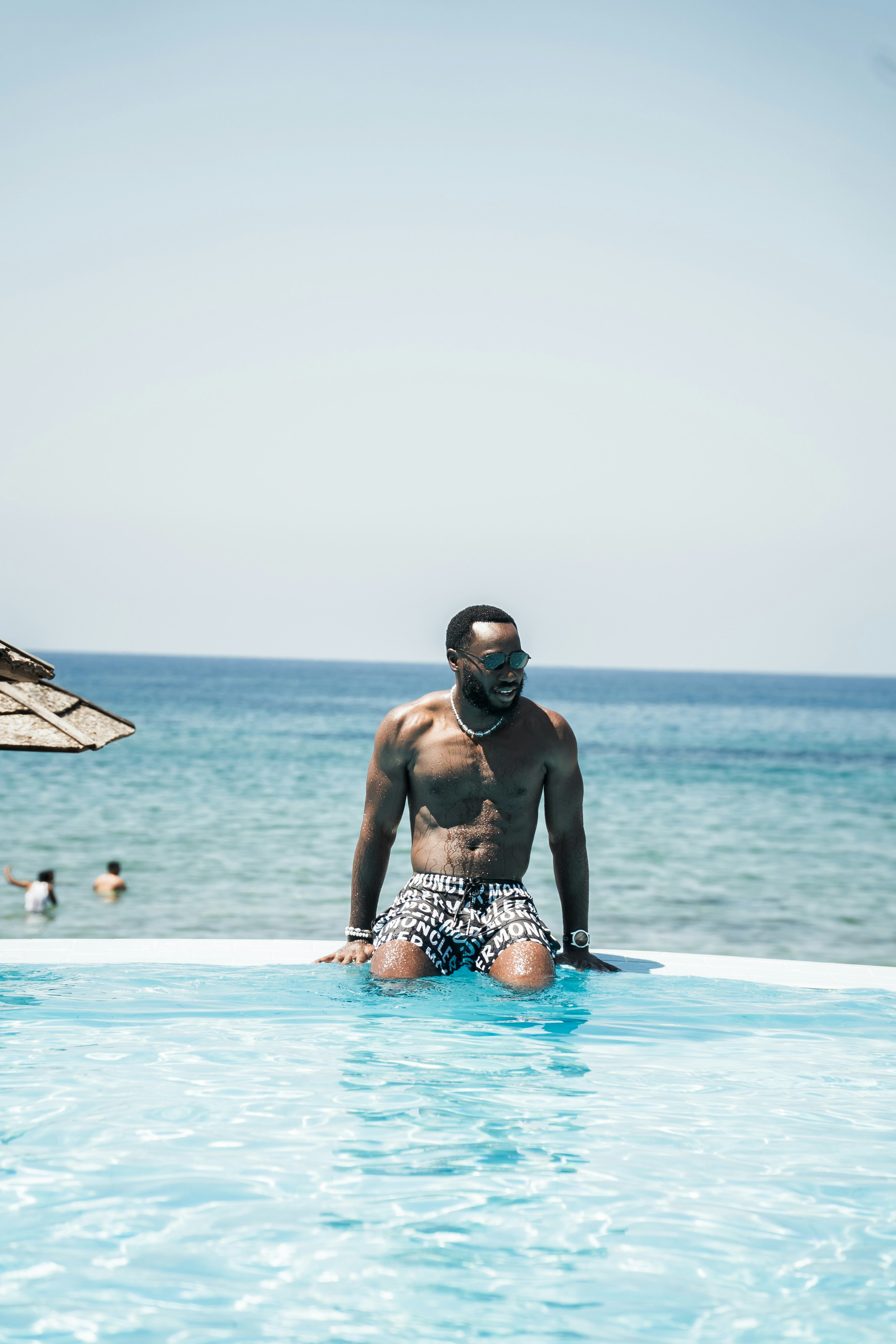 Man kneels by the pool, enjoying the ocean view.