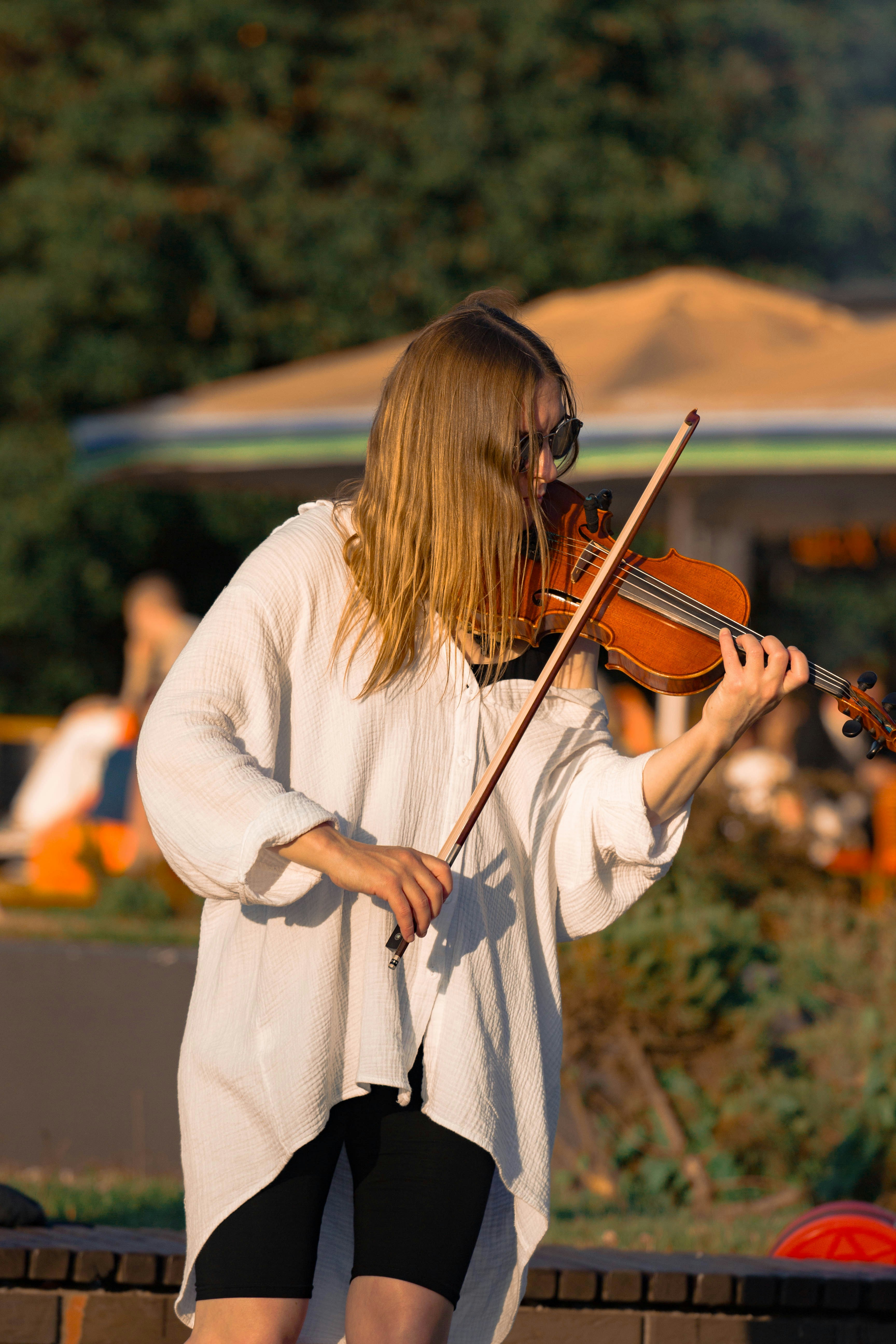 Young woman playing violin in golden sunset light, Taken during performance in outdoor venue. Perfect for art, street culture theme.