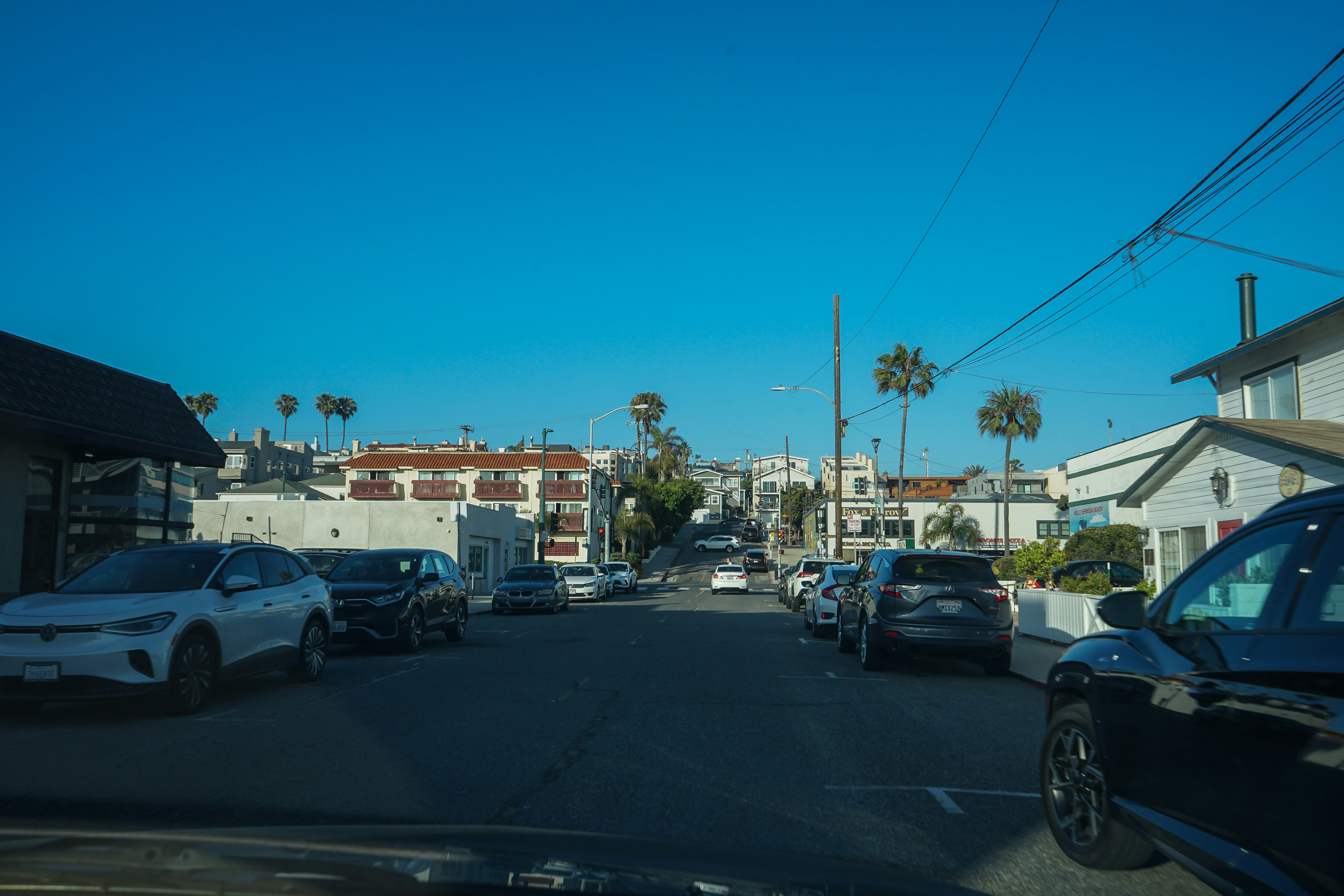 Street with parked cars and buildings on a sunny day.