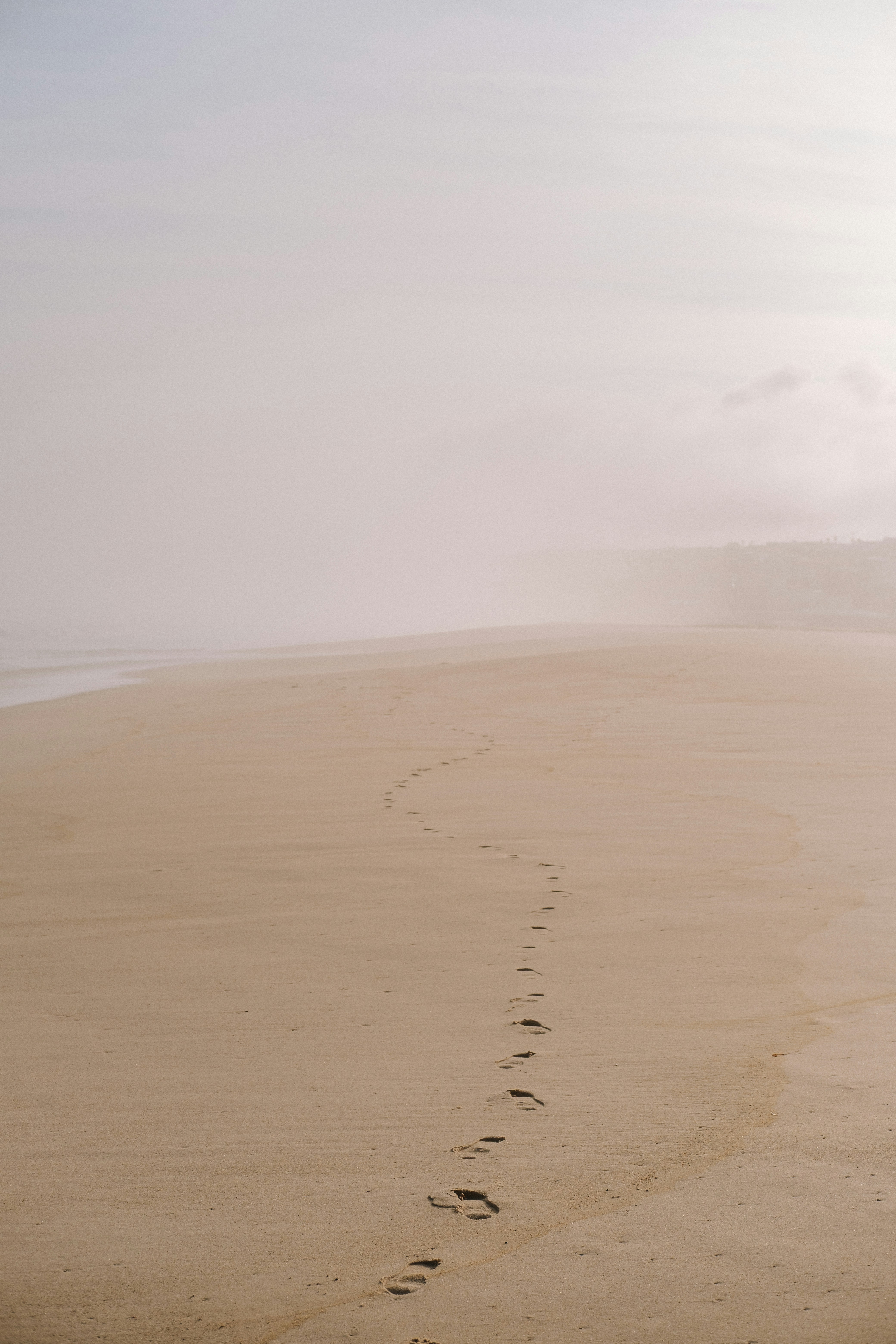 Footprints lead down a foggy beach.
