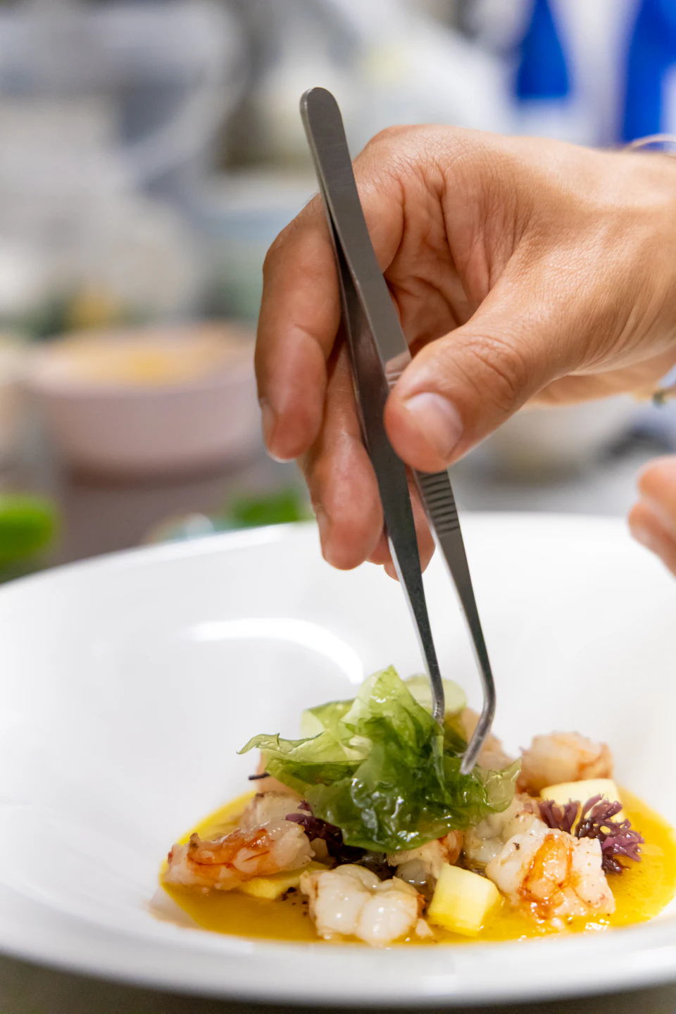 Hand holding tongs poised to pick up food from a white plate on countertop