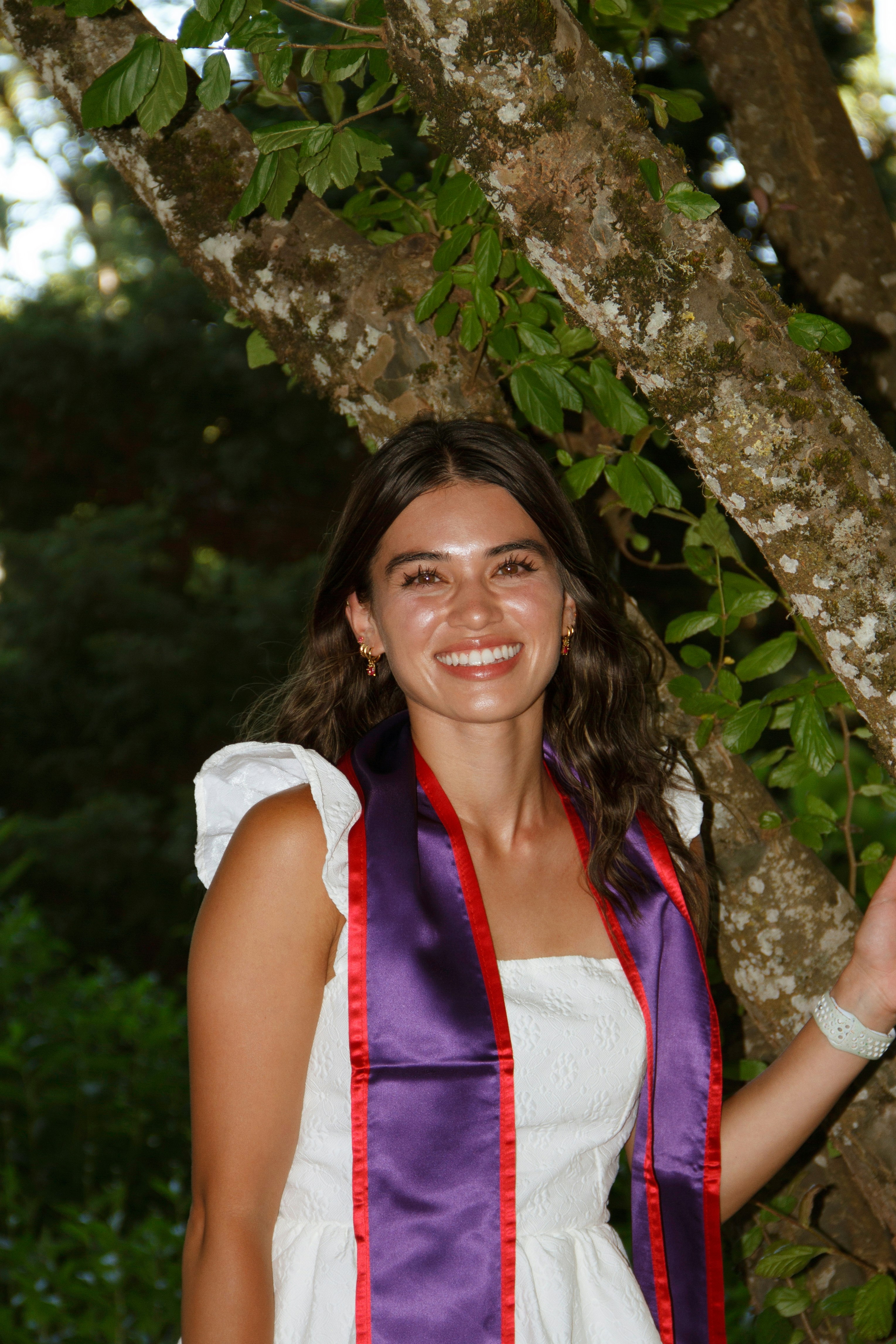 Smiling graduate poses proudly by a tree.