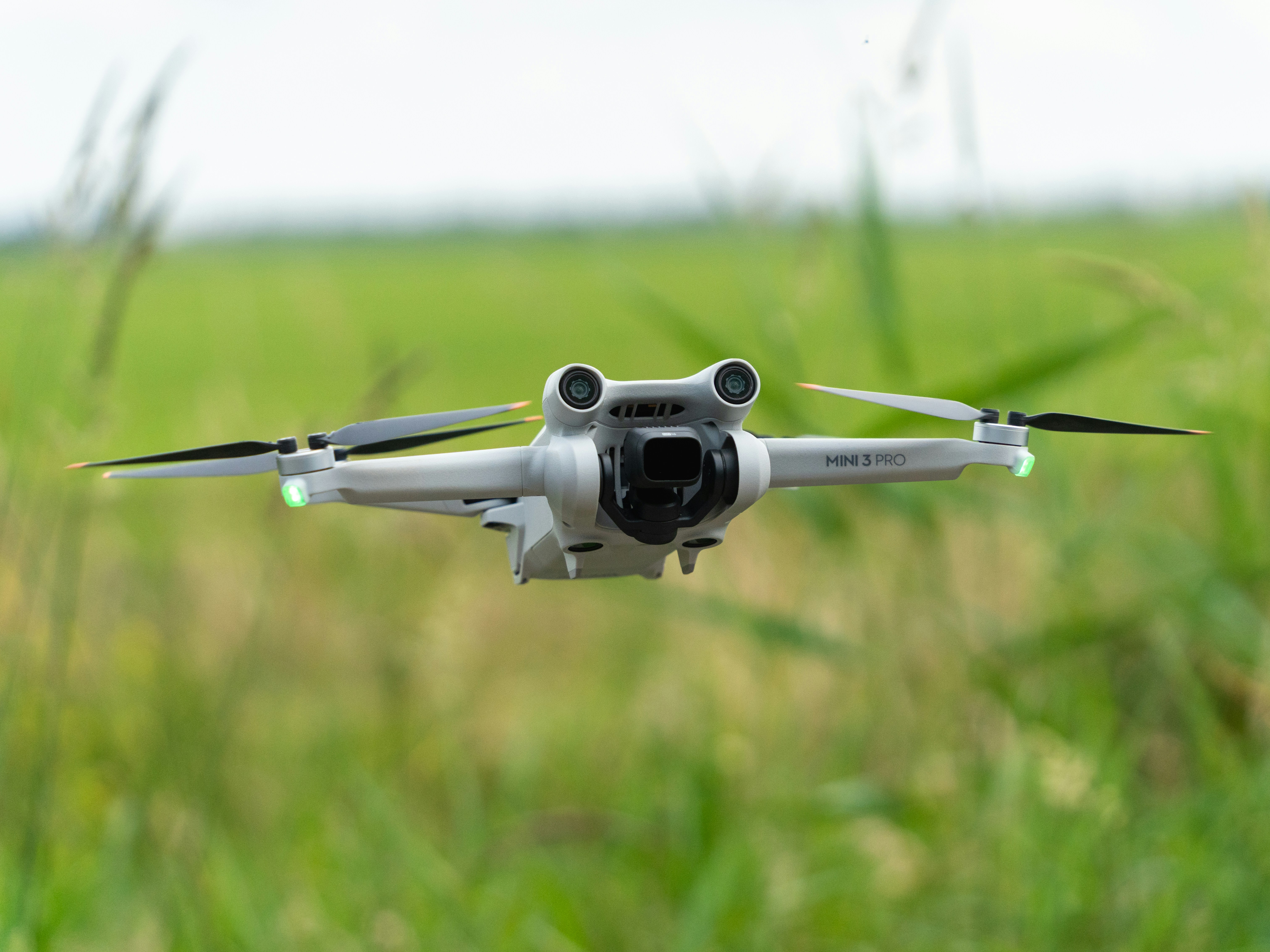 A drone is flying in front of a green field.