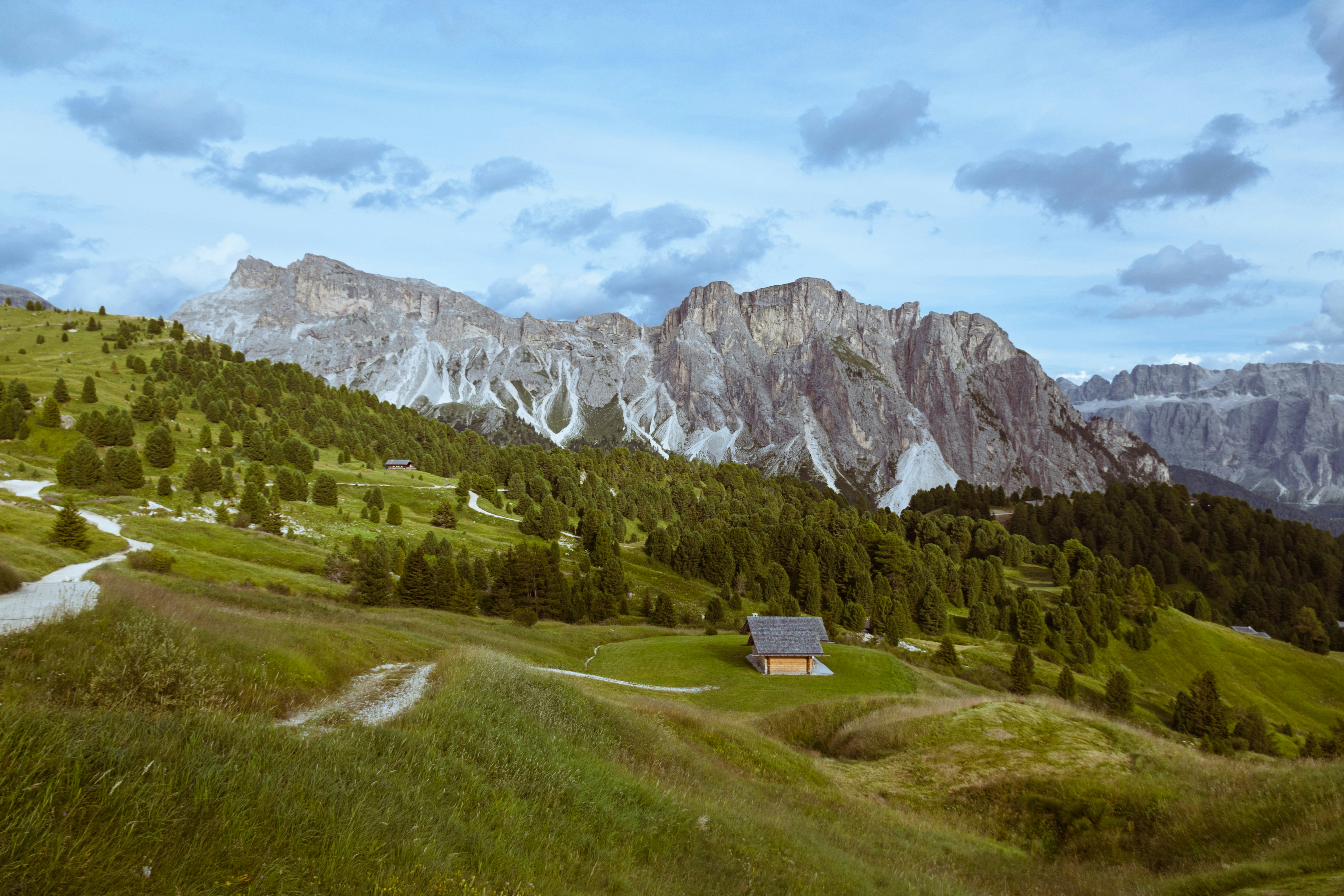 Mountains loom over a grassy landscape with a small house.