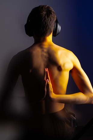 Meditating shirtless man with headphones on.