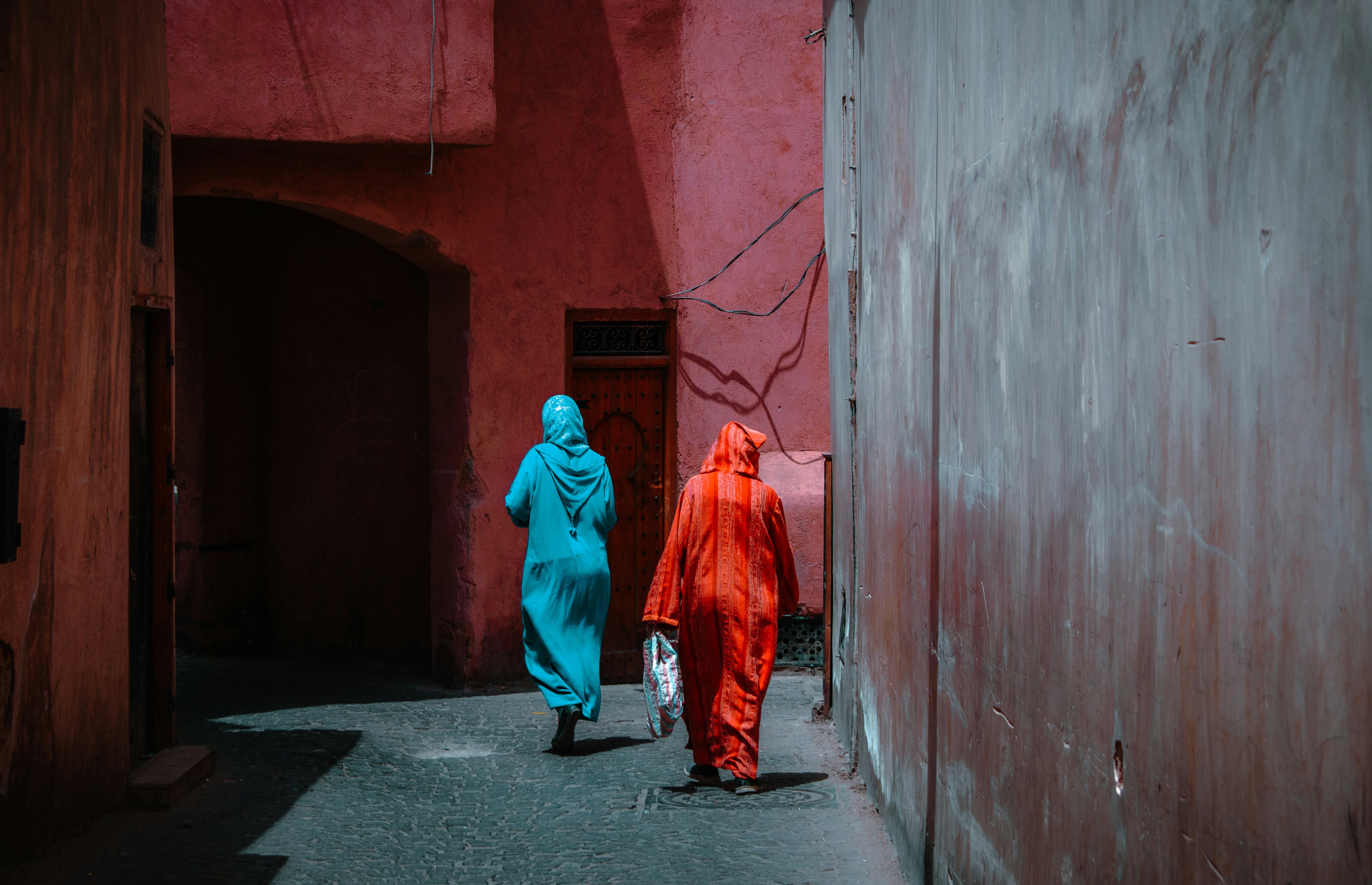 Due figure camminano lungo un vicolo dalle pareti rosa.