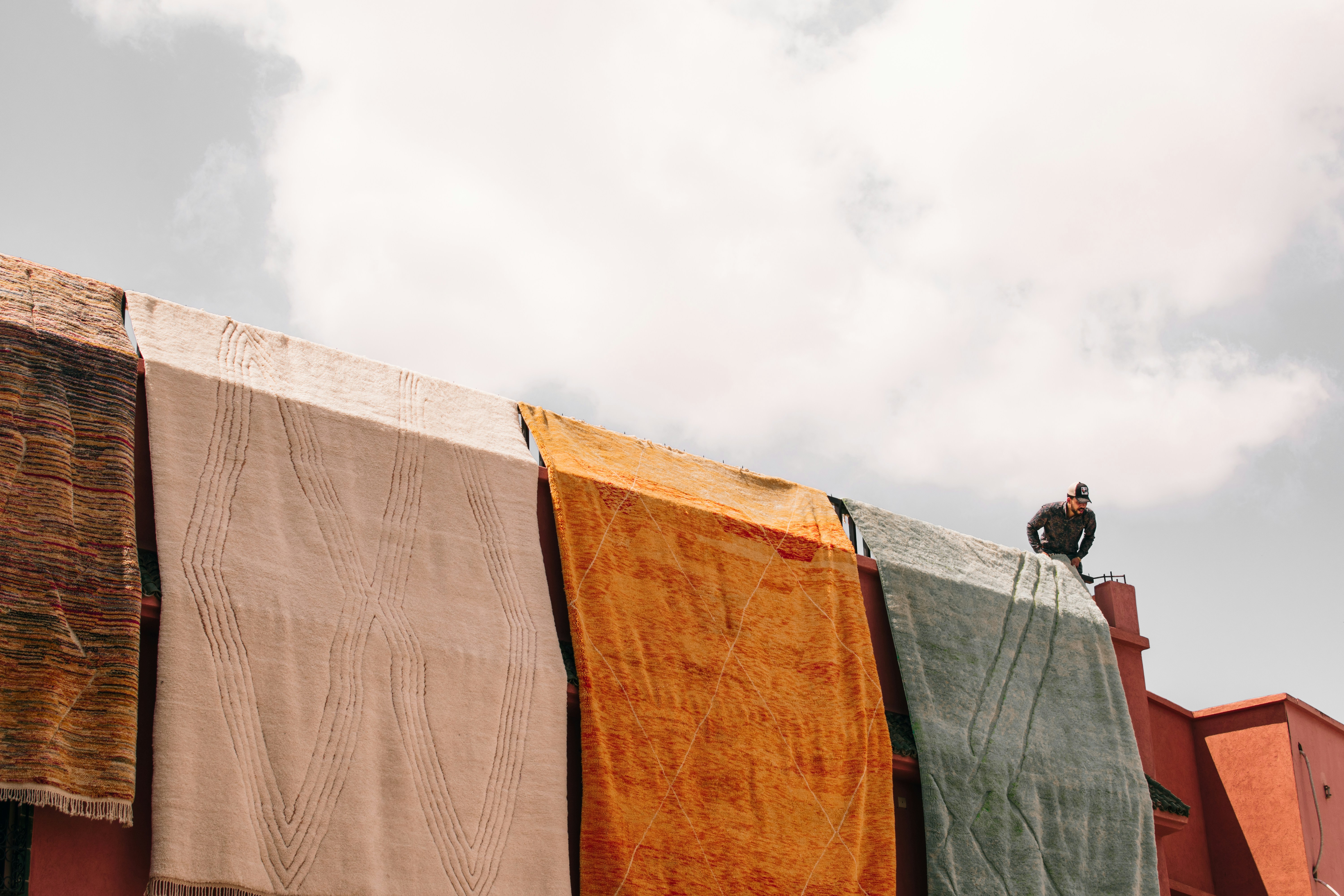 Colorful rugs hang on a rooftop, drying in the sun