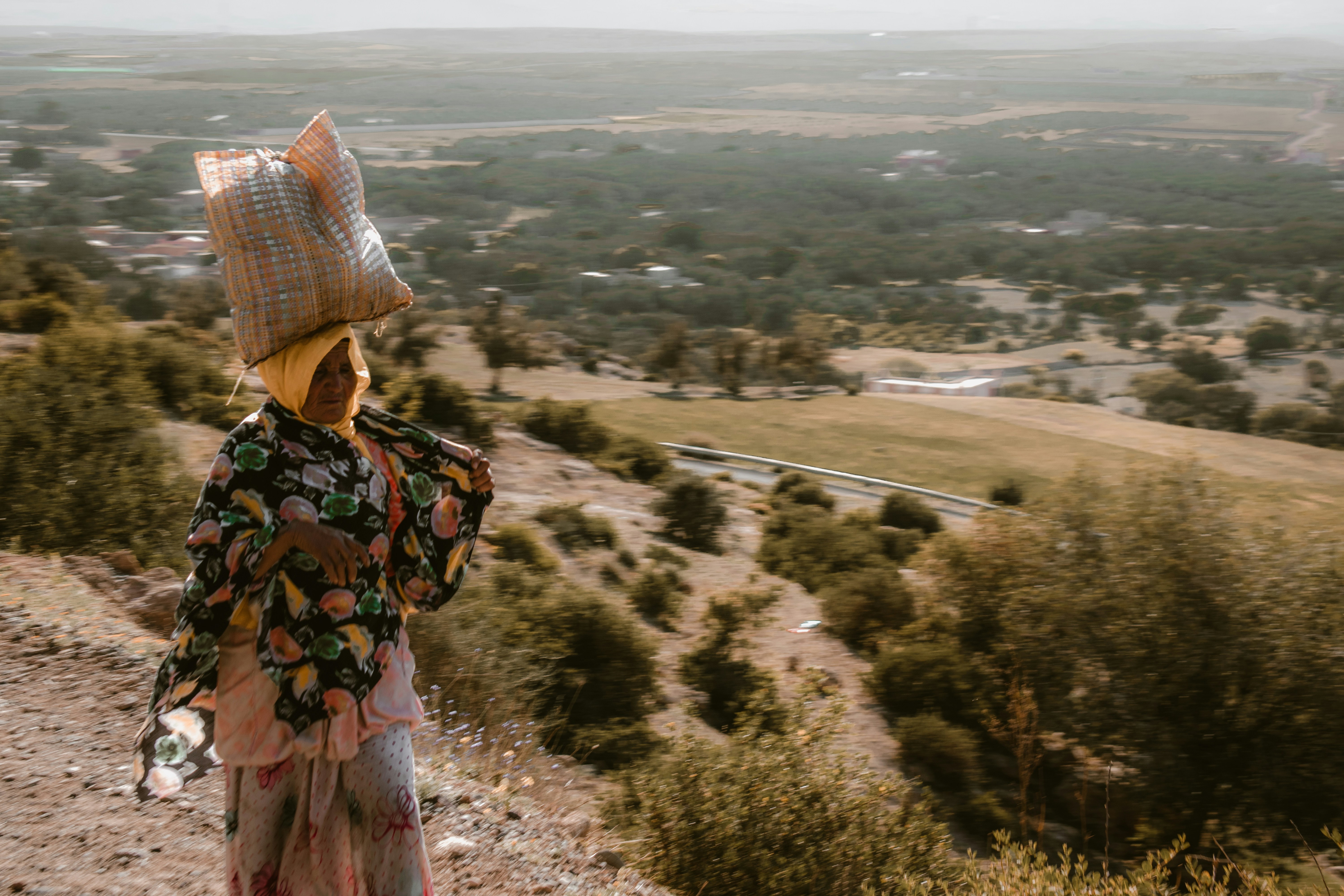 A woman carries a load across a hillside.