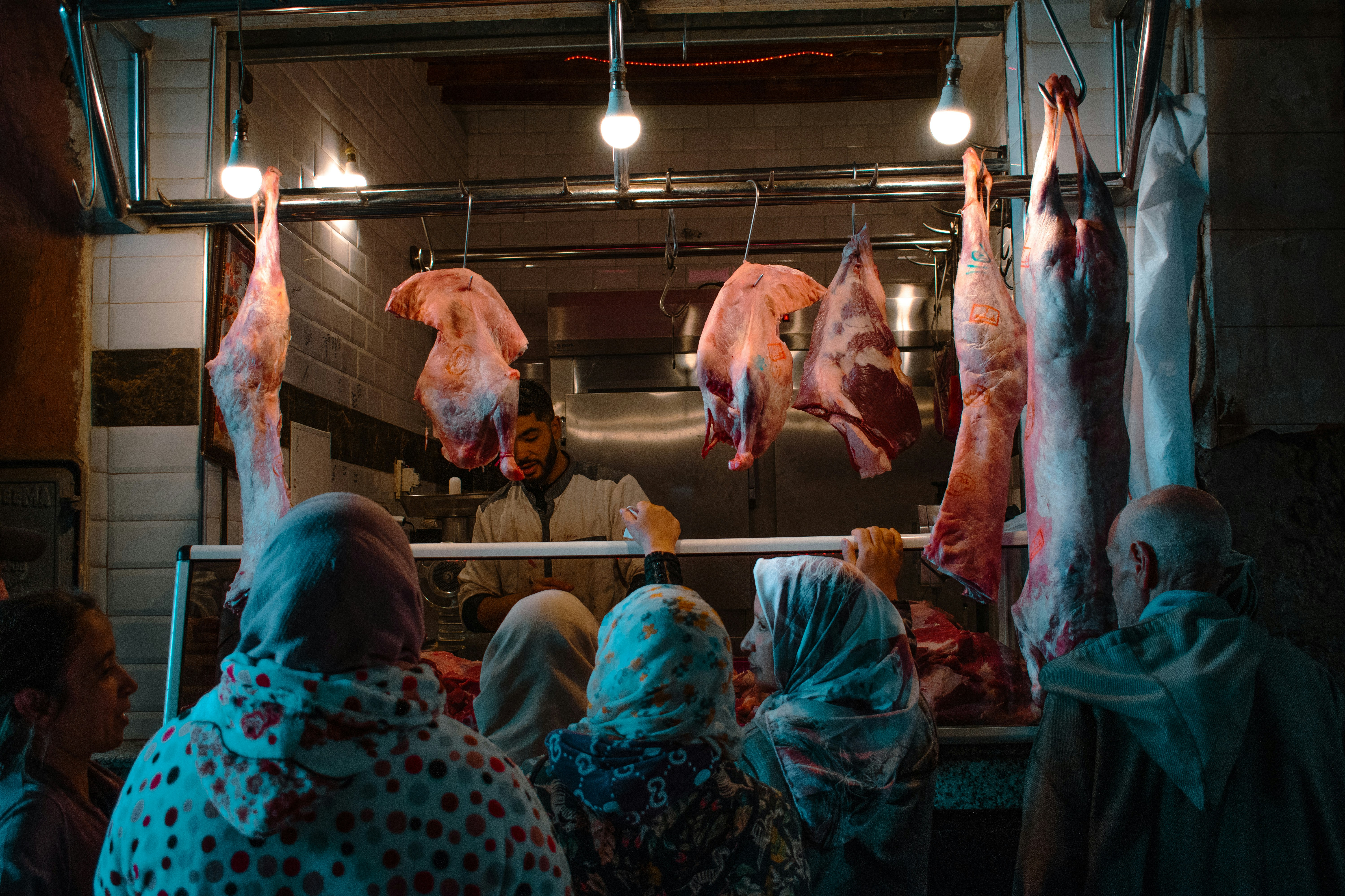 People browse meat hanging at a butcher shop.