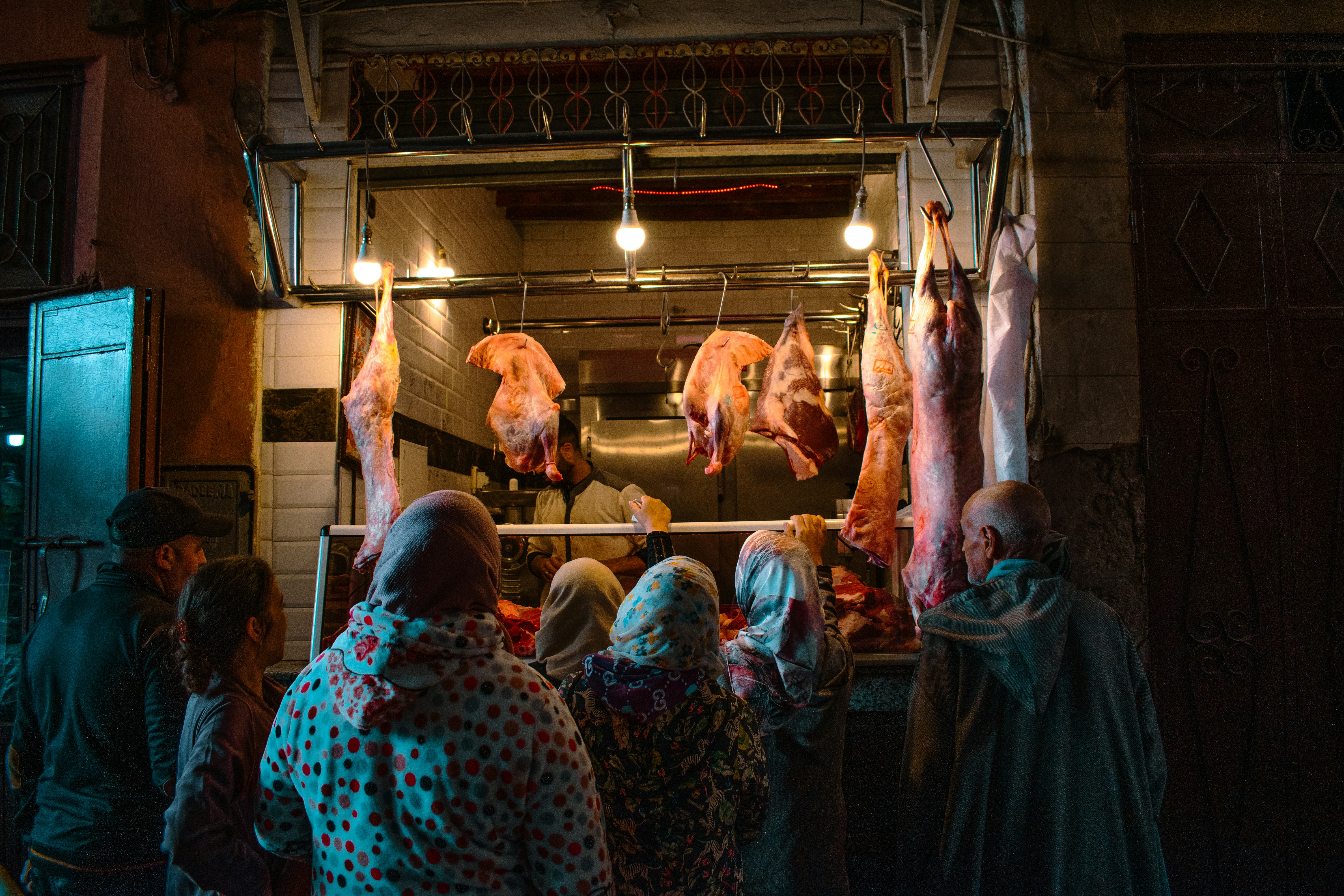 La gente si riunisce per vedere la carne appesa in una macelleria.