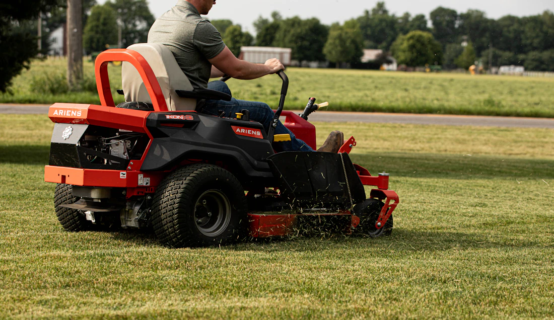 Landscaper on a zero-turn mower cutting a lawn, clippings flying