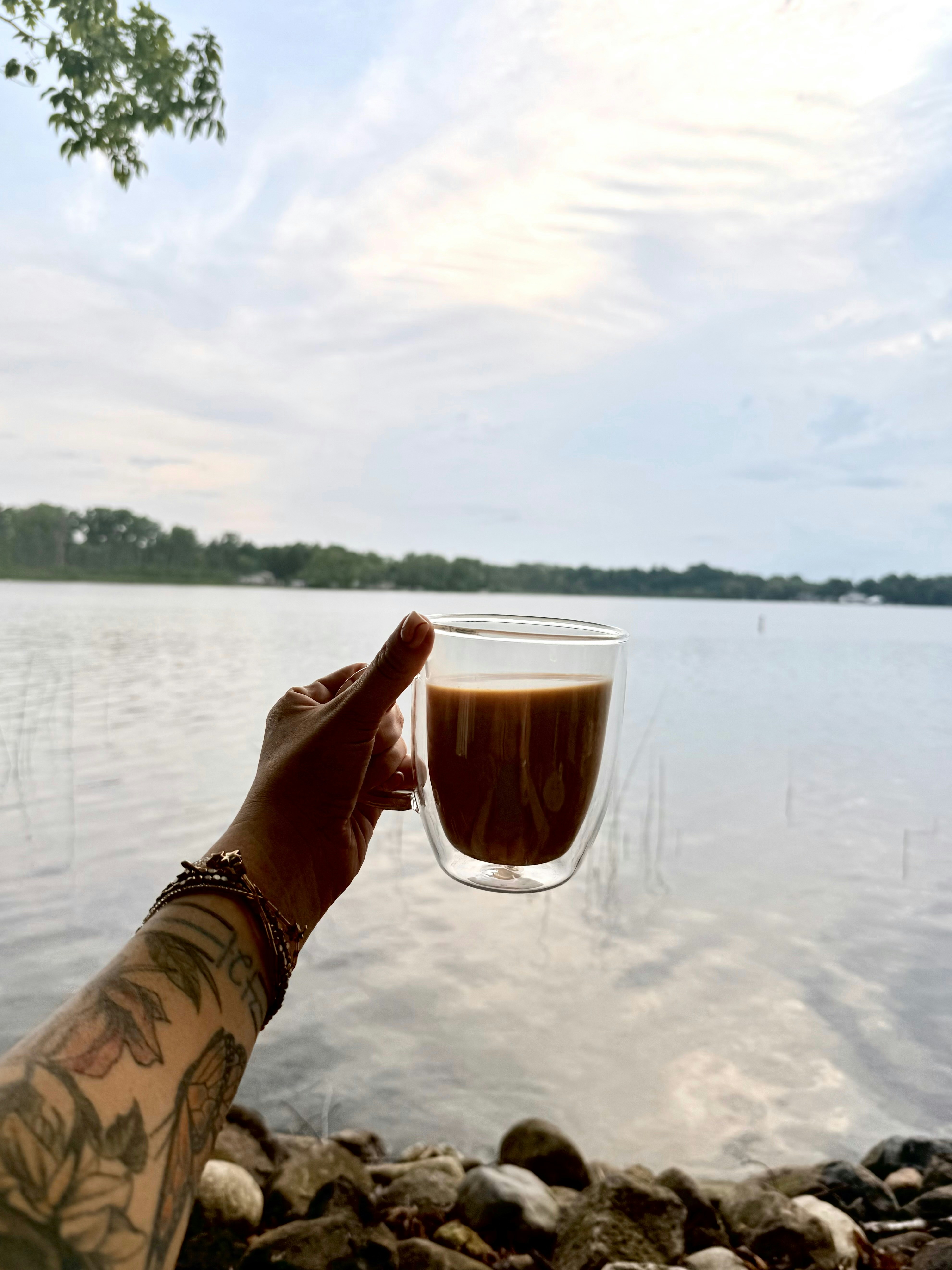 Hand holding coffee in front of a lake.