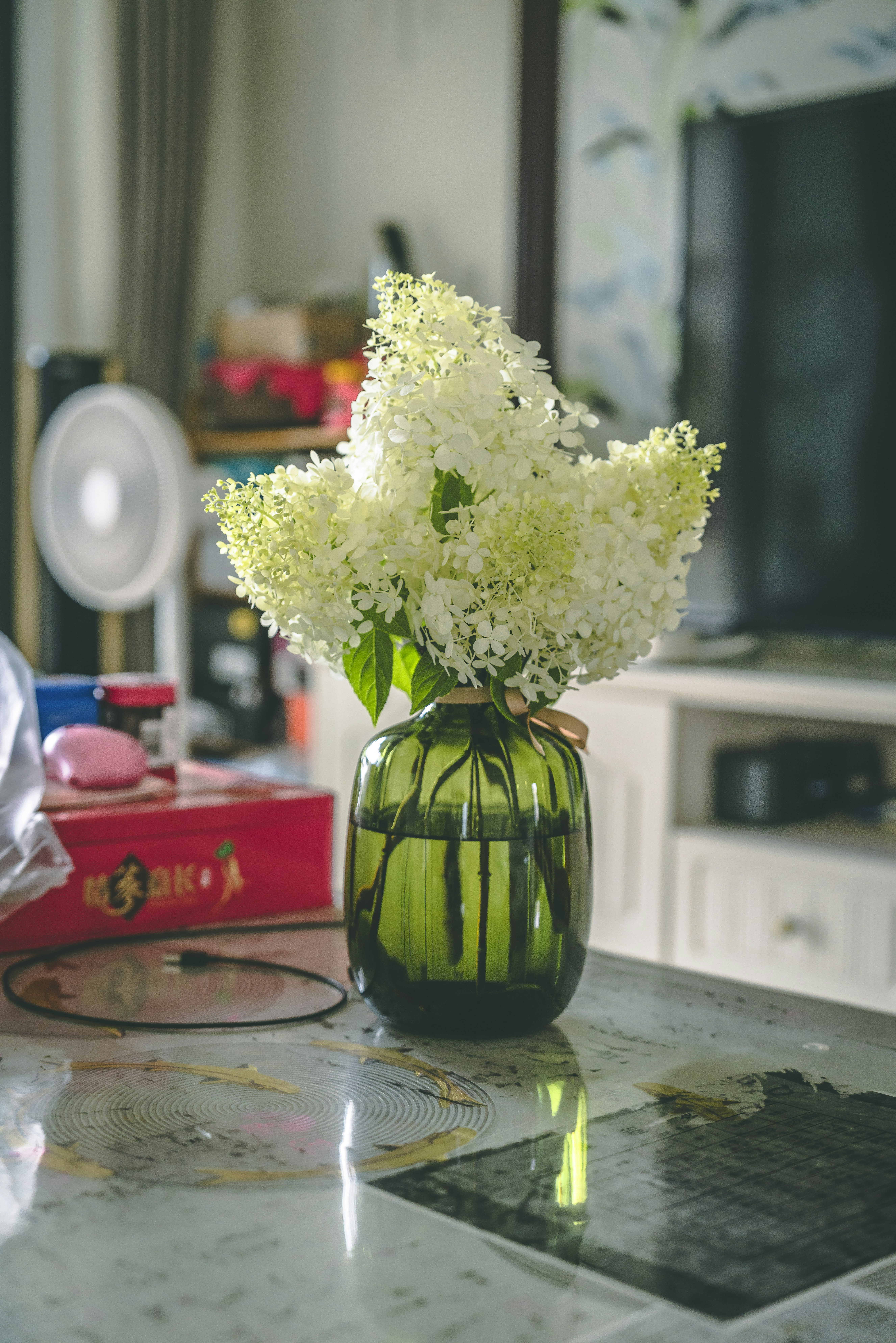 White flowers in a green vase decorate a table.