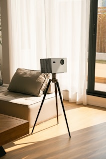 A projector sits on a tripod near a window.