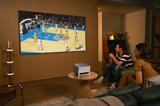 People watch a basketball game on a large screen.