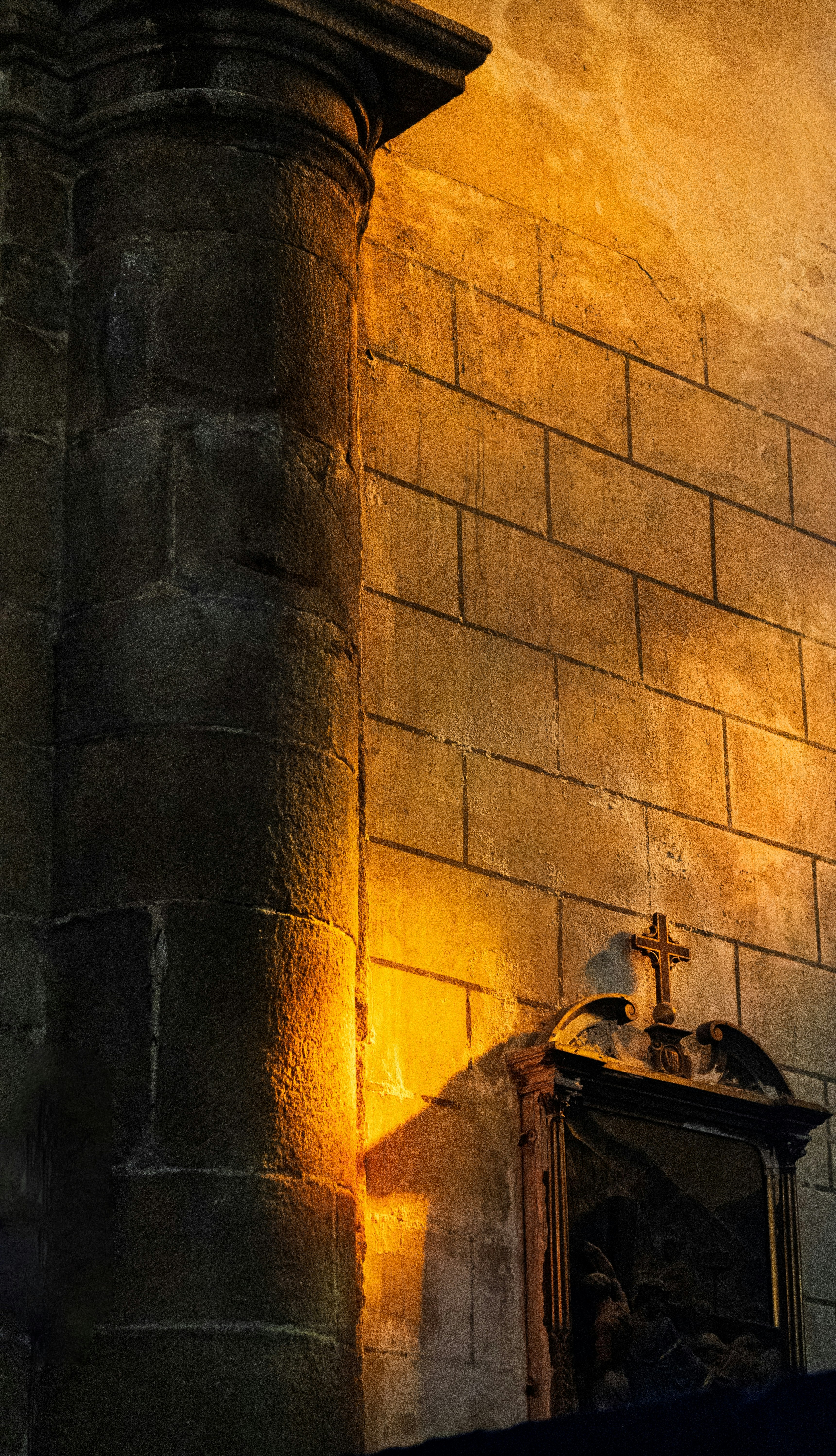 A sunlit pillar casts a shadow on a stone wall.