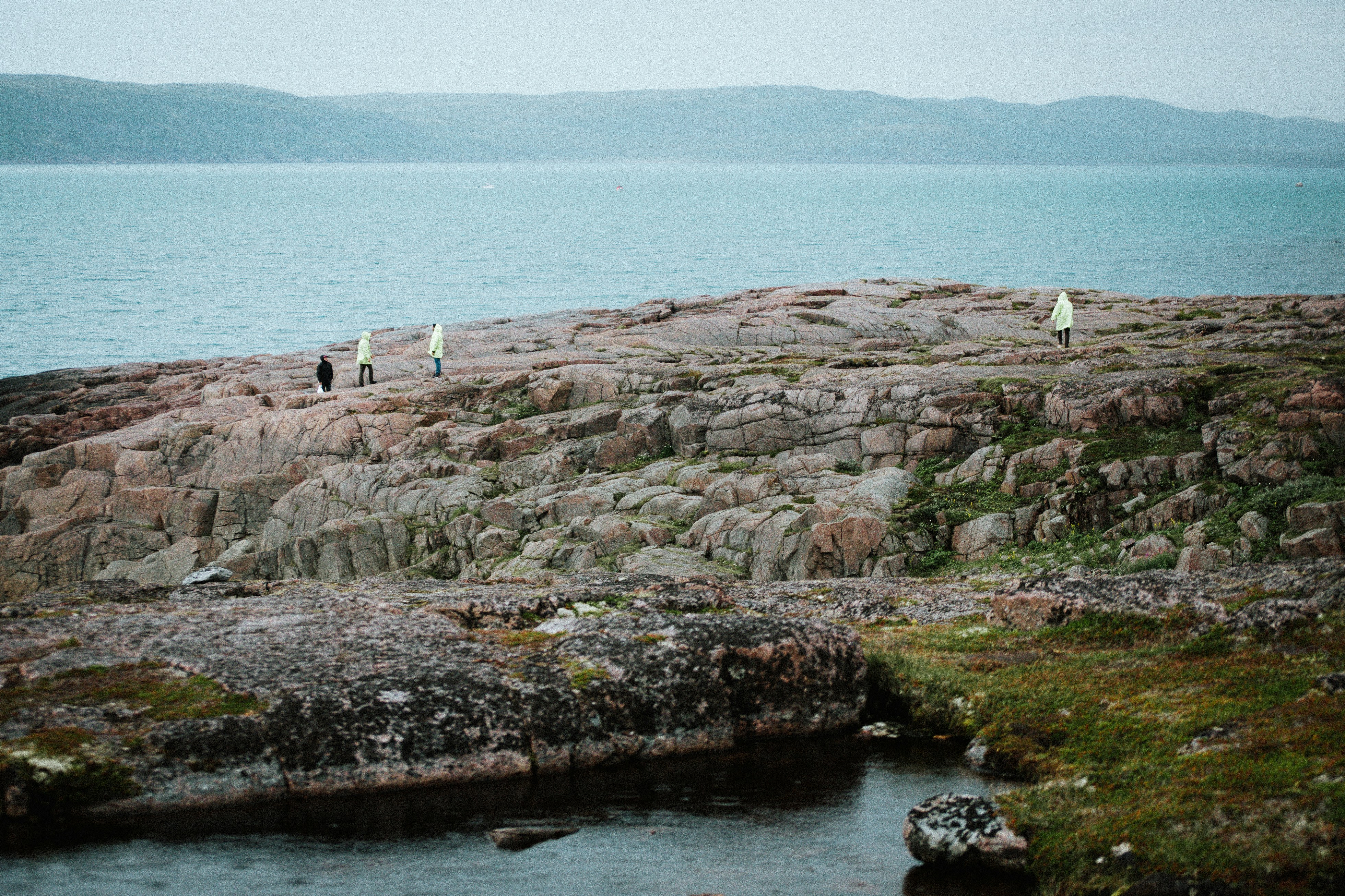 People walk on a rocky coast near the ocean.