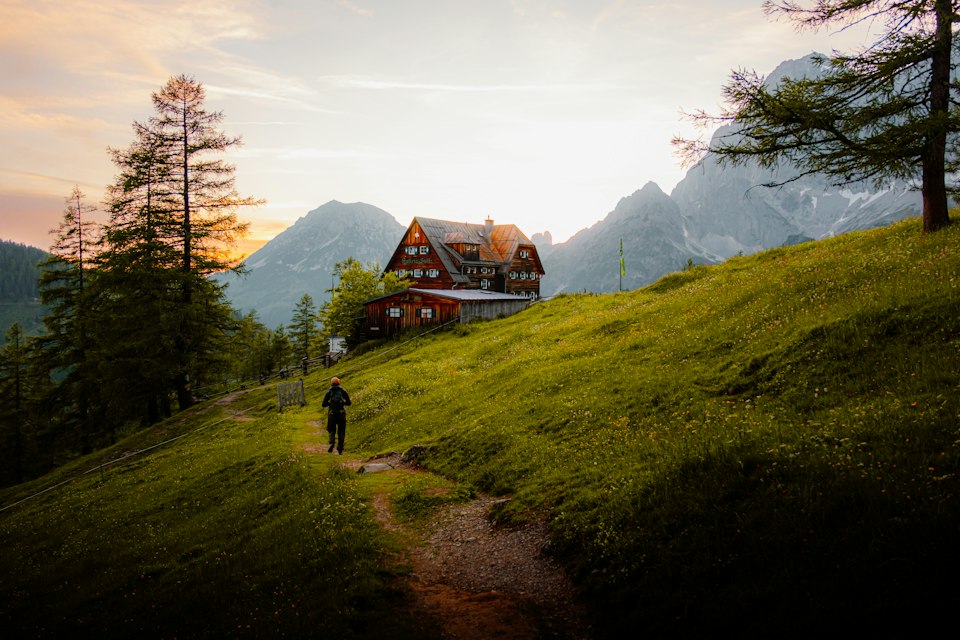 A hiker approaching a traditional wooden alpine hut at dusk in the Austrian Alps