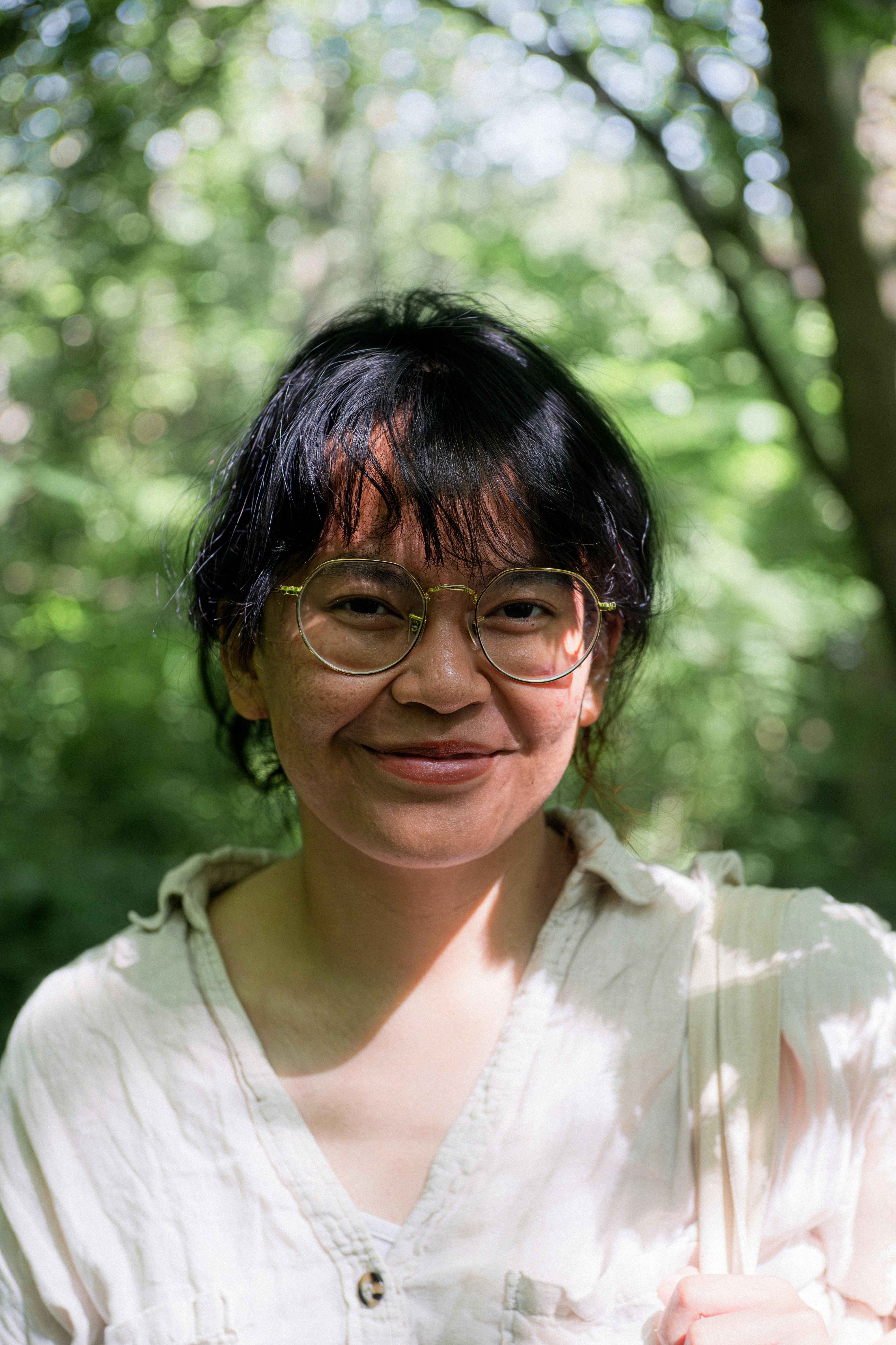 Una donna con gli occhiali sorride in mezzo al fogliame.